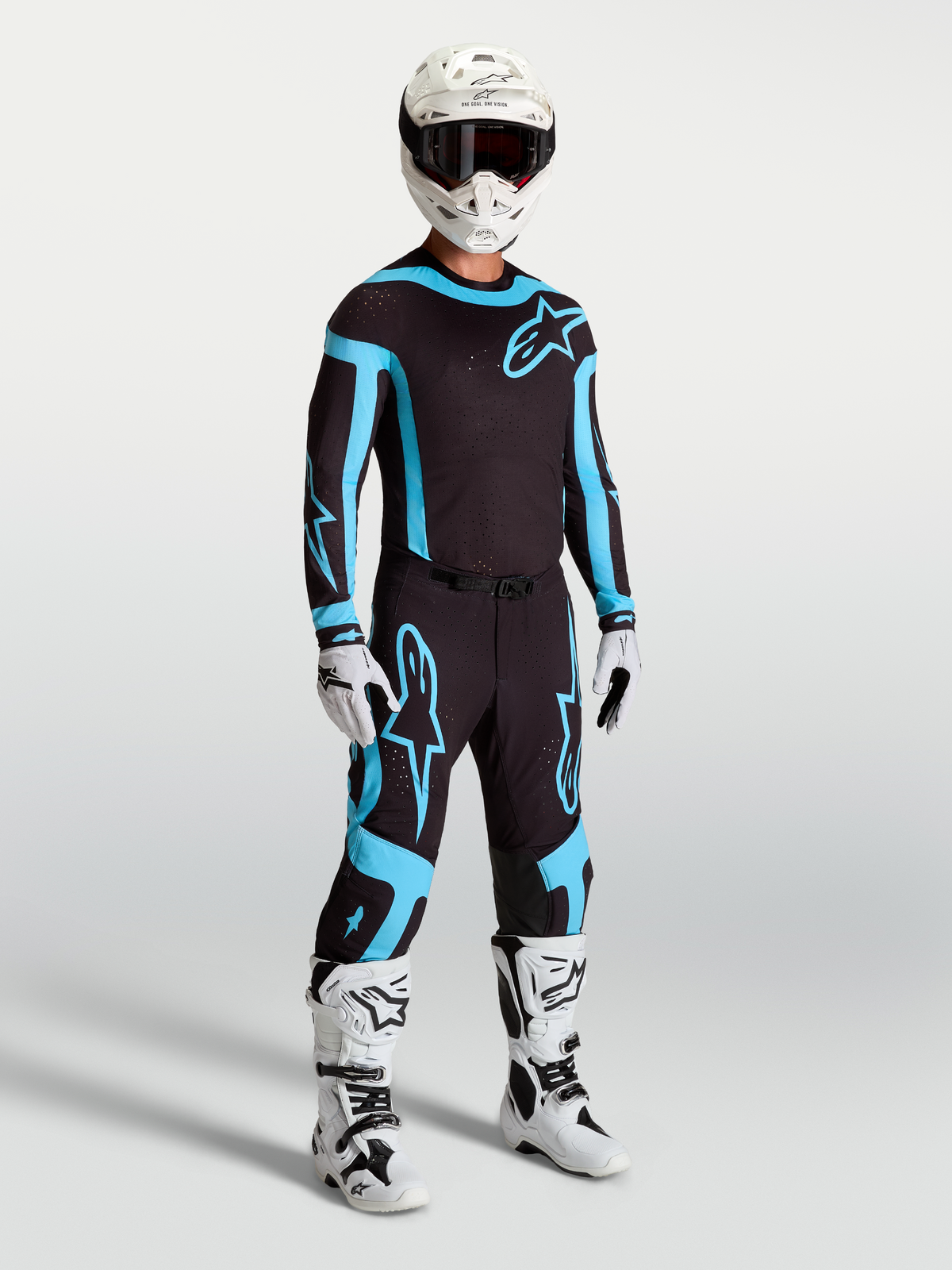 Spodnie Supertech Vesta Alpinestars, męskie spodnie motocrossowe, czarne i turkusowe, profesjonalna odzież wyścigowa z białymi butami i kaskiem.