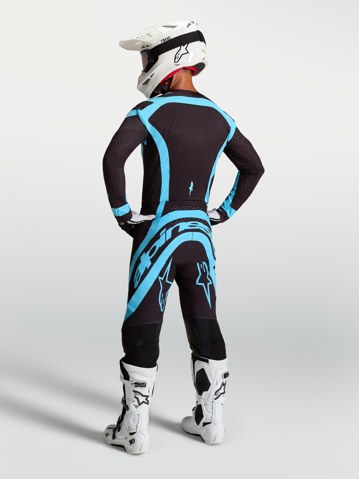 Spodnie Alpinestars Supertech Vesta, profesjonalne spodnie motocrossowe, czarne i turkusowe, widok z tyłu na modelu, wykonane z elastycznego materiału rip-stop, odzież do jazdy terenowej.