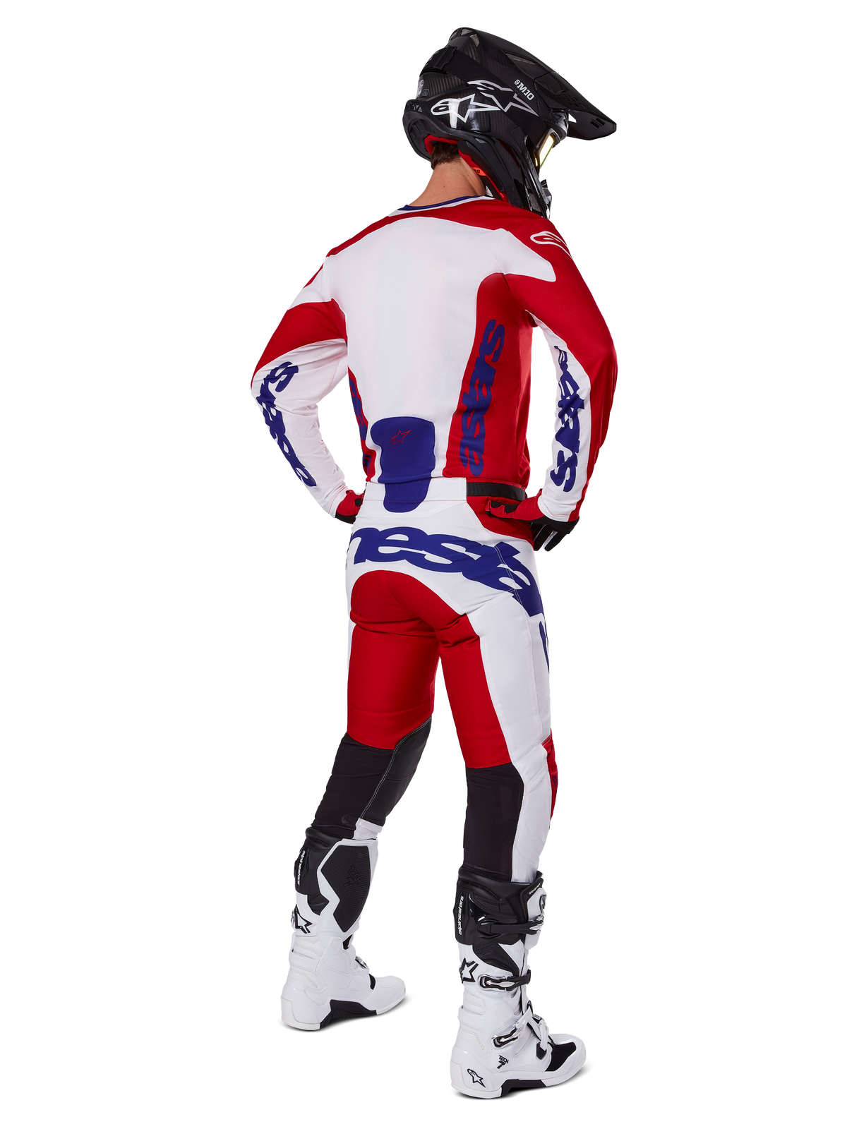 Alpinestars Racer Veil Pants 2025, spodnie motocrossowe, jaskrawoczerwone i białe z niebieskimi akcentami, widok od tyłu na motocyklistę w pełnym stroju, wyraźne logo Alpinestars, oddychające panele na dolnej części nogawek, białe buty i czarny kask