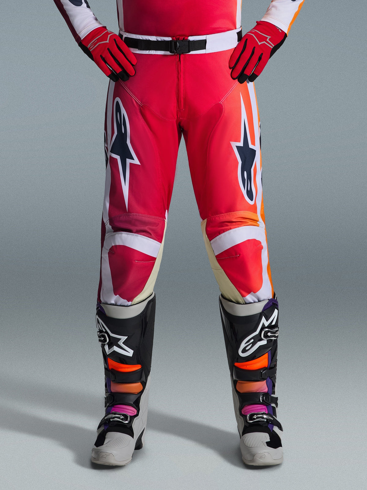 Alpinestars 2026 Racer Portl Pants, spodnie motocrossowe, czerwone, jasnoszare i ciemnoszare, noszone z pasującymi czerwonymi rękawicami i wielokolorowymi butami, z wyraźnymi logotypami gwiazdy Alpinestars na udach i białymi akcentami, sportowy design do wyścigów off-road