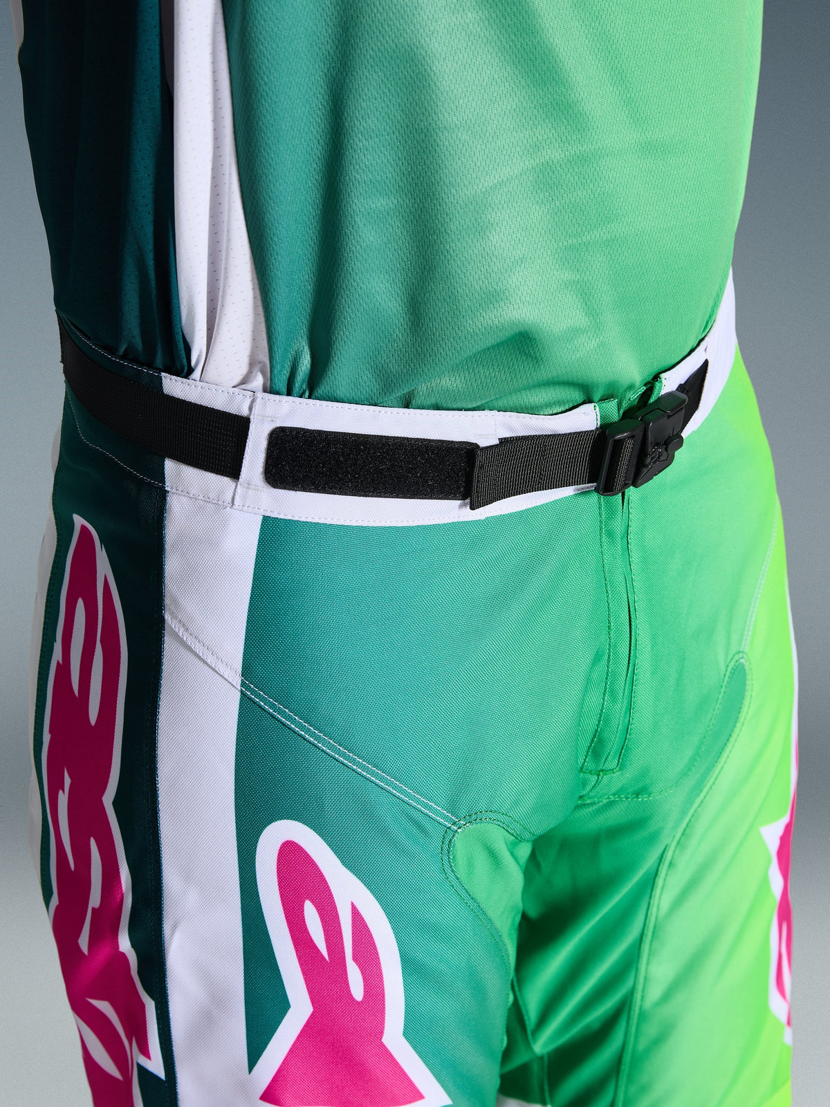 Spodnie Alpinestars 2026 Racer Portl, spodnie motocrossowe, zielone, białe i czarne z różowymi akcentami logo, zbliżenie na pas pokazujące magnetyczną klamrę SX2 i regulowane zapięcie, wytrzymały sprzęt do wyścigów off-road