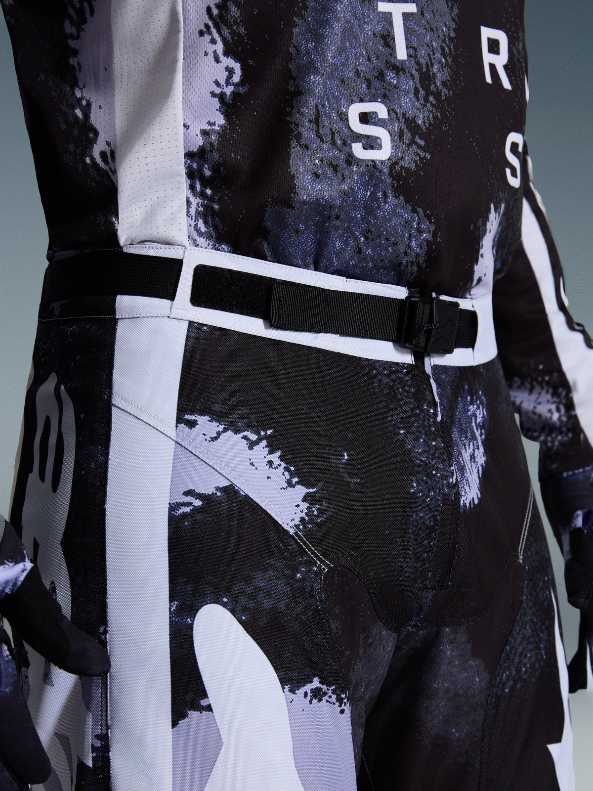 Alpinestars 2026 Racer Lahnd Pants, spodnie motocrossowe w kolorze Iron Camo, zbliżenie na regulowany pas i magnetyczną klamrę SX2, szaro-czarny wzór kamuflażu i wytrzymała konstrukcja z materiału polyfabric 600D.