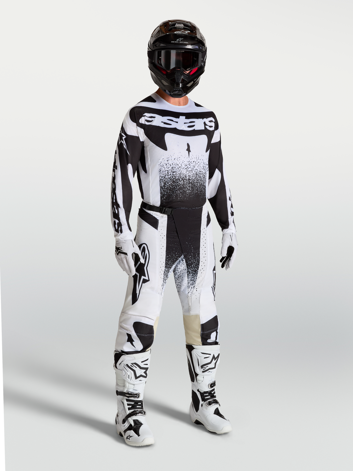 Spodnie Alpinestars Techstar Swan, męskie spodnie motocrossowe, czarne i białe, sportowy krój wyścigowy, elastyczny materiał ripstop, model w pełnym zestawie odzieży wyścigowej z kaskiem i butami.