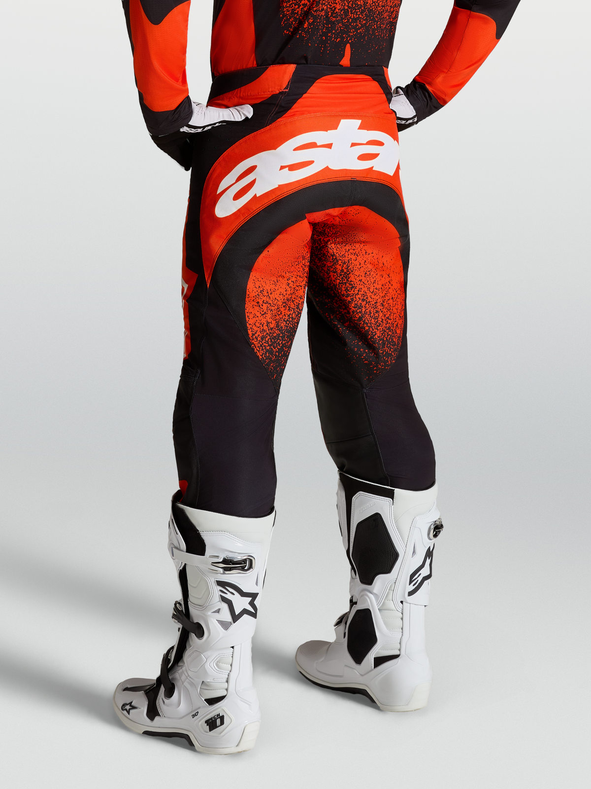 Alpinestars Spodnie Techstar Swan, męskie spodnie motocrossowe, czerwono-czarne, biały napis Astar na siedzeniu, na modelu z butami Tech 10.