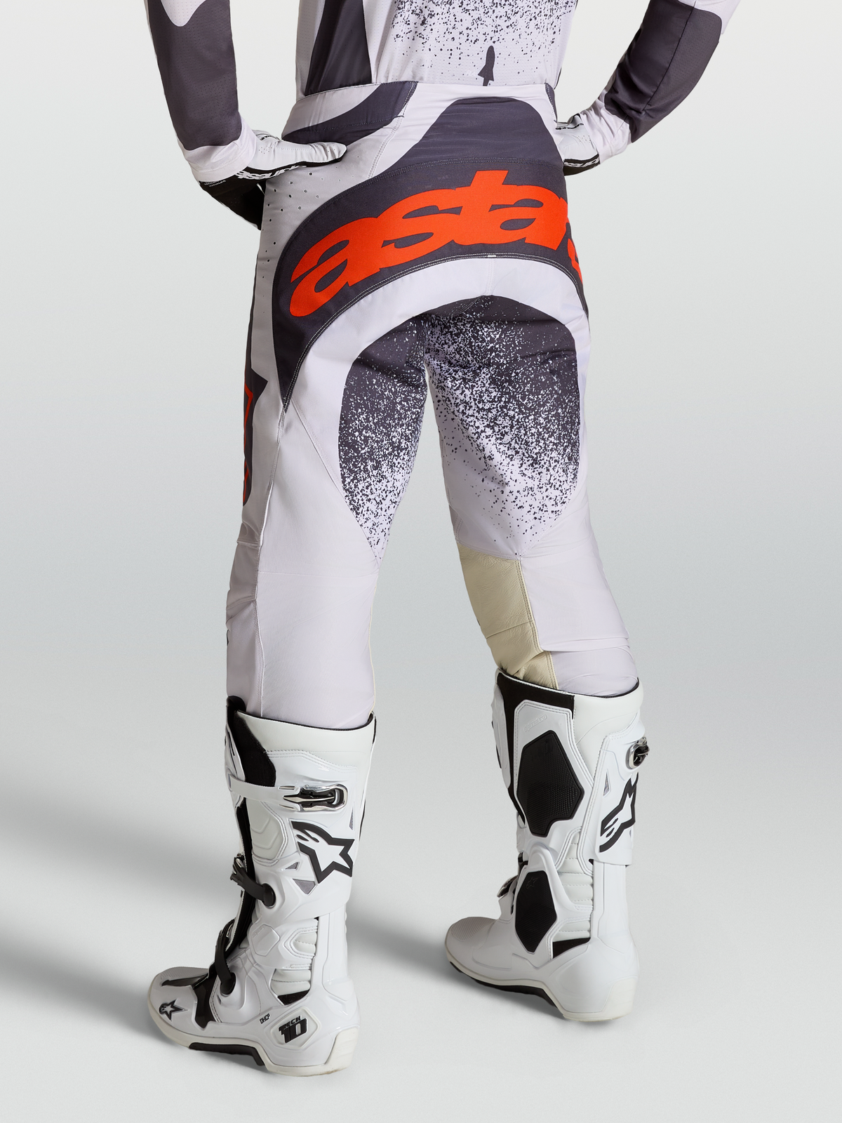 Alpinestars Spodnie Techstar Swan, spodnie motocrossowe męskie, jasnoliliowe i ciemnoszare z czerwonymi akcentami fluo, buty Tech 10, tył podkreślający panel siedziska 600D.