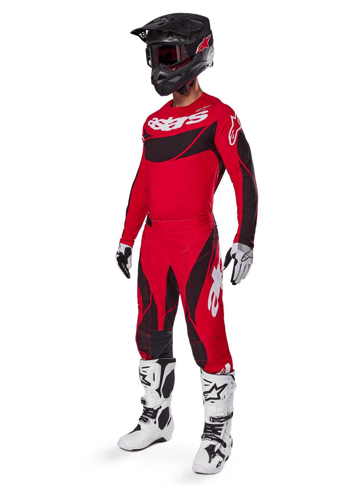 Motocyklista motocrossowy w kompletnym stroju wyścigowym Alpinestars, spodnie Techstar Dreem 2025 w kolorze jasnoczerwonym i czarnym, pasująca czerwono-czarna koszulka z białym logo, czarny kask oraz biało-czarne buty, skoordynowany zestaw do wyścigów terenowych