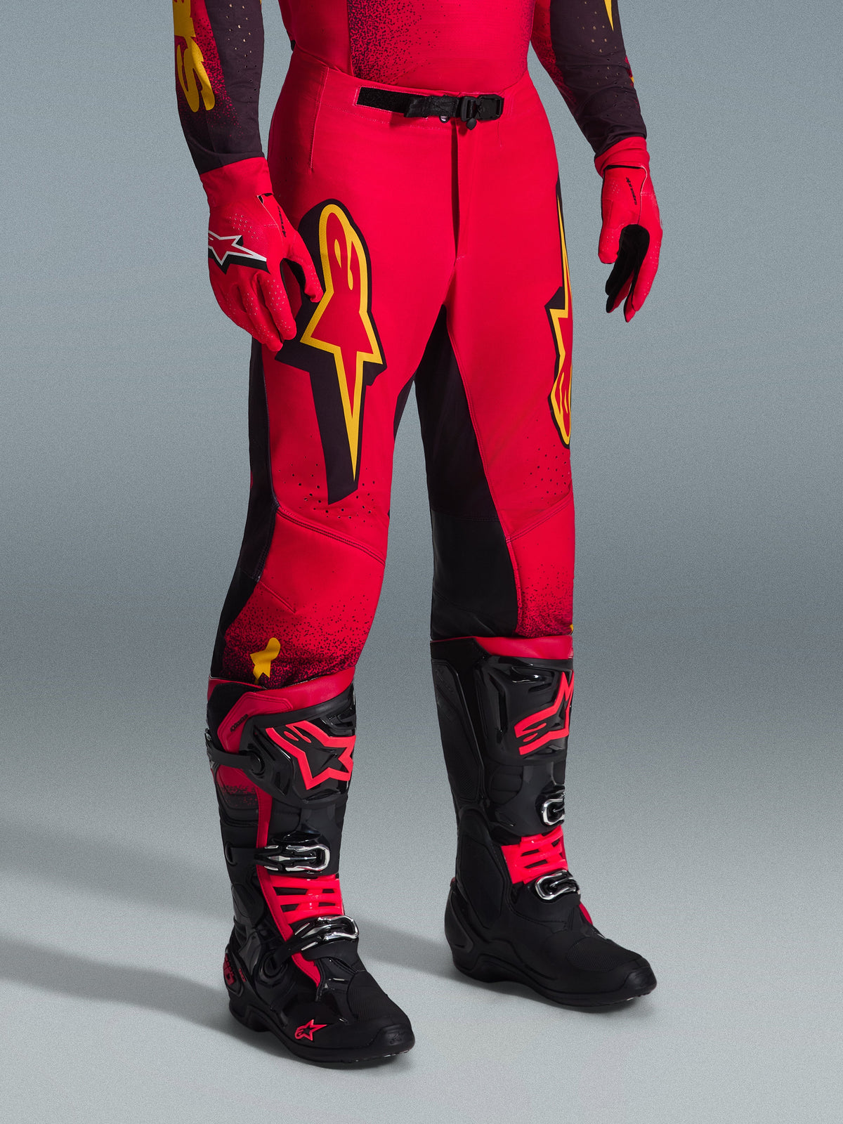 Alpinestars 2026 Supertech Scenz Pants, spodnie motocrossowe, czerwone, czarne i żółte, z żółtymi logotypami Alpinestars i czarnymi panelami, noszone z pasującą czerwoną koszulką, czerwonymi rękawicami i czarnymi butami motocrossowymi.