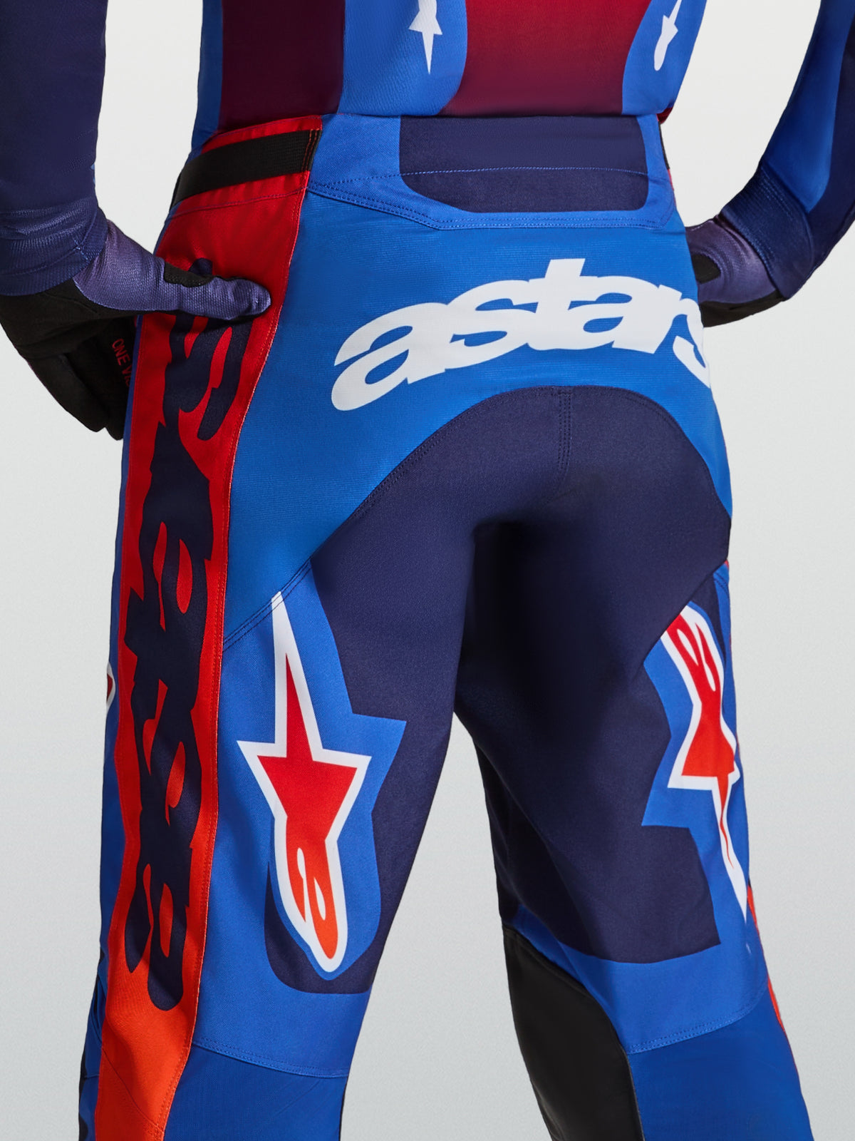Alpinestars Racer Hunt, męskie spodnie motocrossowe, niebieskie i czerwone, logo astars i grafika gwiazdy, widok z tyłu.