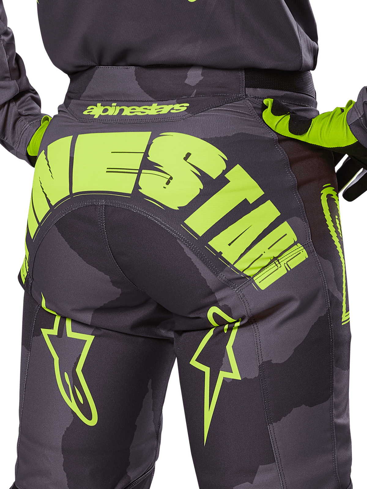 Alpinestars 2025 Racer Hollow Pants, spodnie motocrossowe, kolor ciemne camo i fluorescencyjny żółty, z dużym żółtym logo Alpinestars z tyłu, taktyczny wzór camo z jaskrawymi akcentami, wytrzymała konstrukcja do wyścigów terenowych