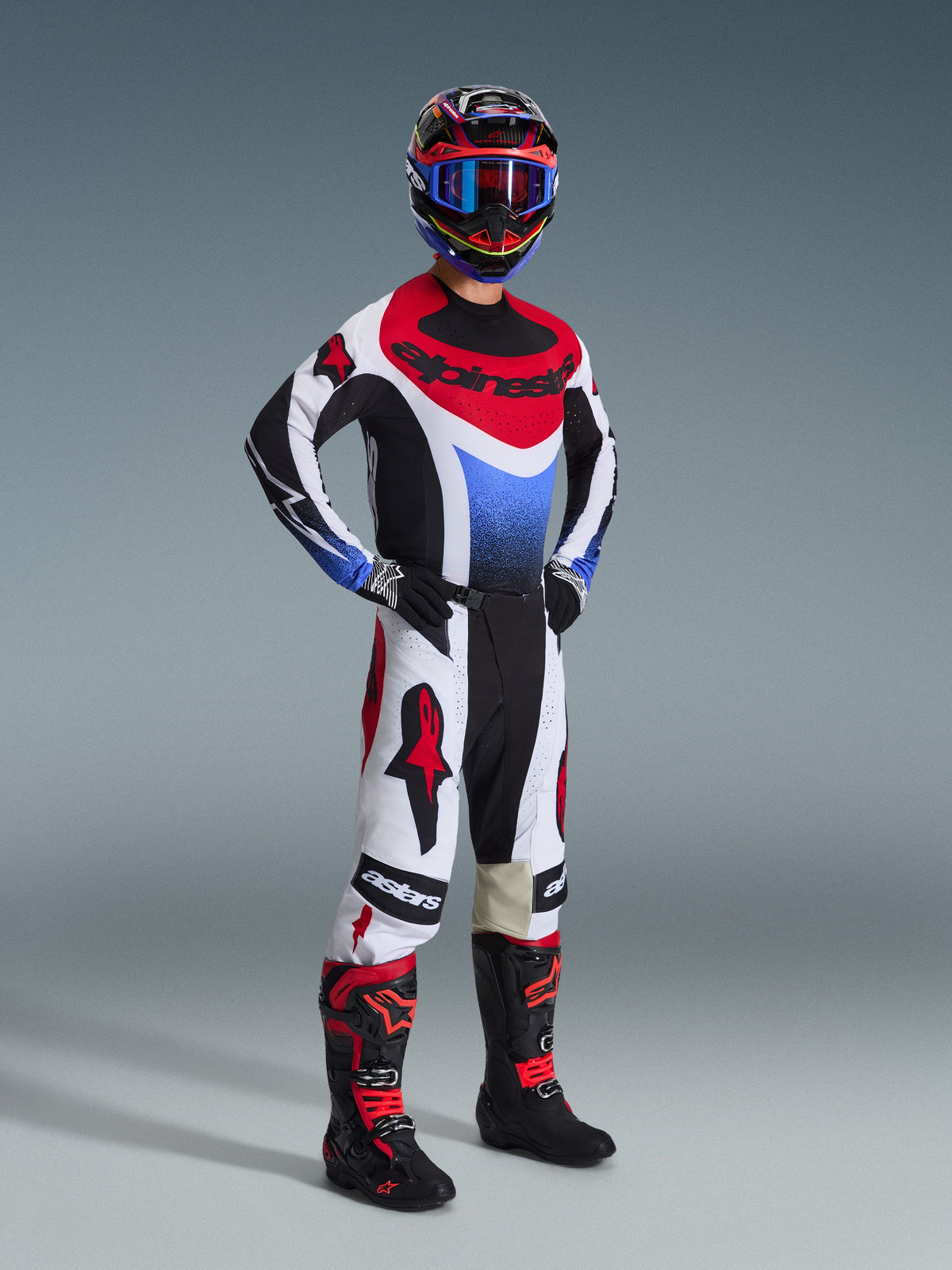 Alpinestars 2026 Techstar Knif Pants, spodnie motocrossowe, czarno-biało-czerwone, prezentowane na zawodniku w pełnym stroju wyścigowym z pasującą bluzą i butami, z wyrazistymi czerwonymi logo Alpinestars na białych panelach, o sportowym kroju.