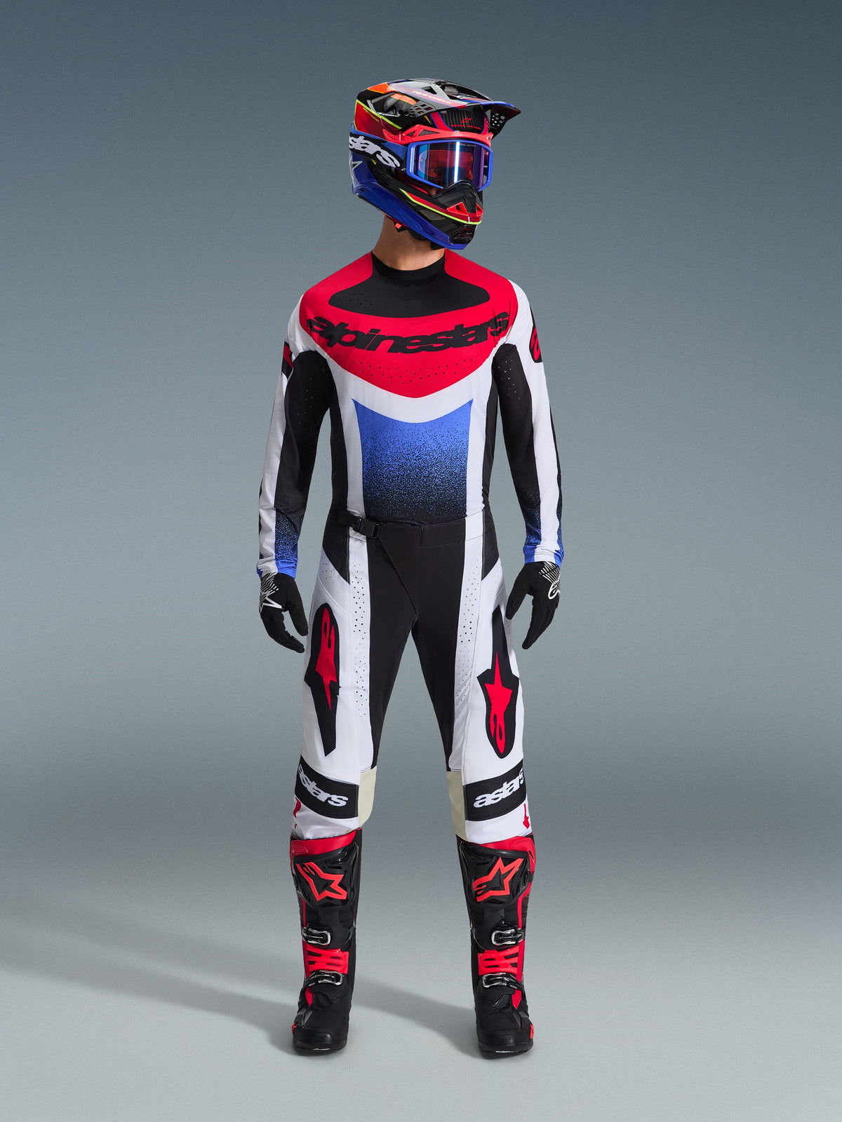 Alpinestars Techstar Knif Pants 2026, spodnie motocrossowe, czarno-biało-czerwone, noszone jako część pełnego zestawu wyścigowego z pasującą koszulką i kaskiem, czerwone logo gwiazdy na udach, dopasowany sportowy krój do wyścigów off-road