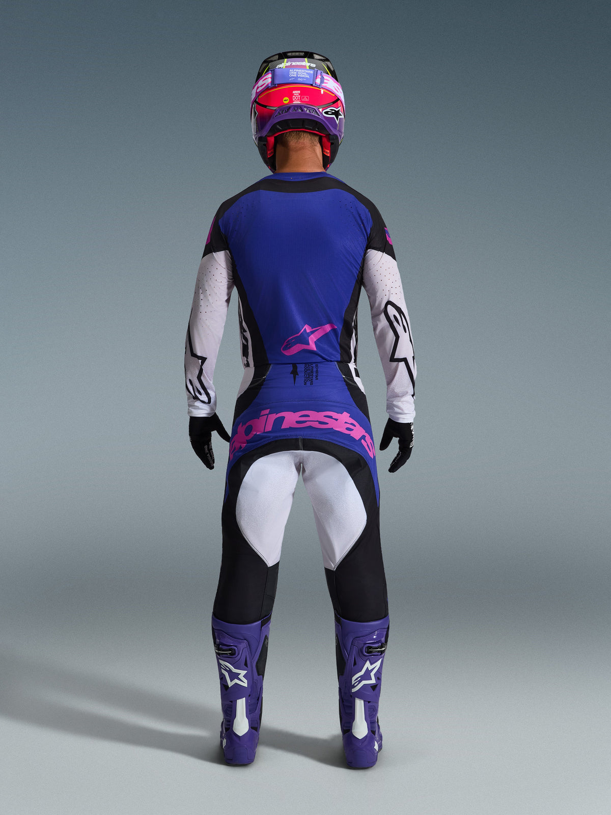 Strój Alpinestars 2026 Techstar Knif, widok z tyłu na motocyklistę motocrossowego, czarny, jasnoszary i fioletowy z różowym logo, ubrany w dopasowane fioletowe buty i kask, profesjonalna odzież wyścigowa off-road