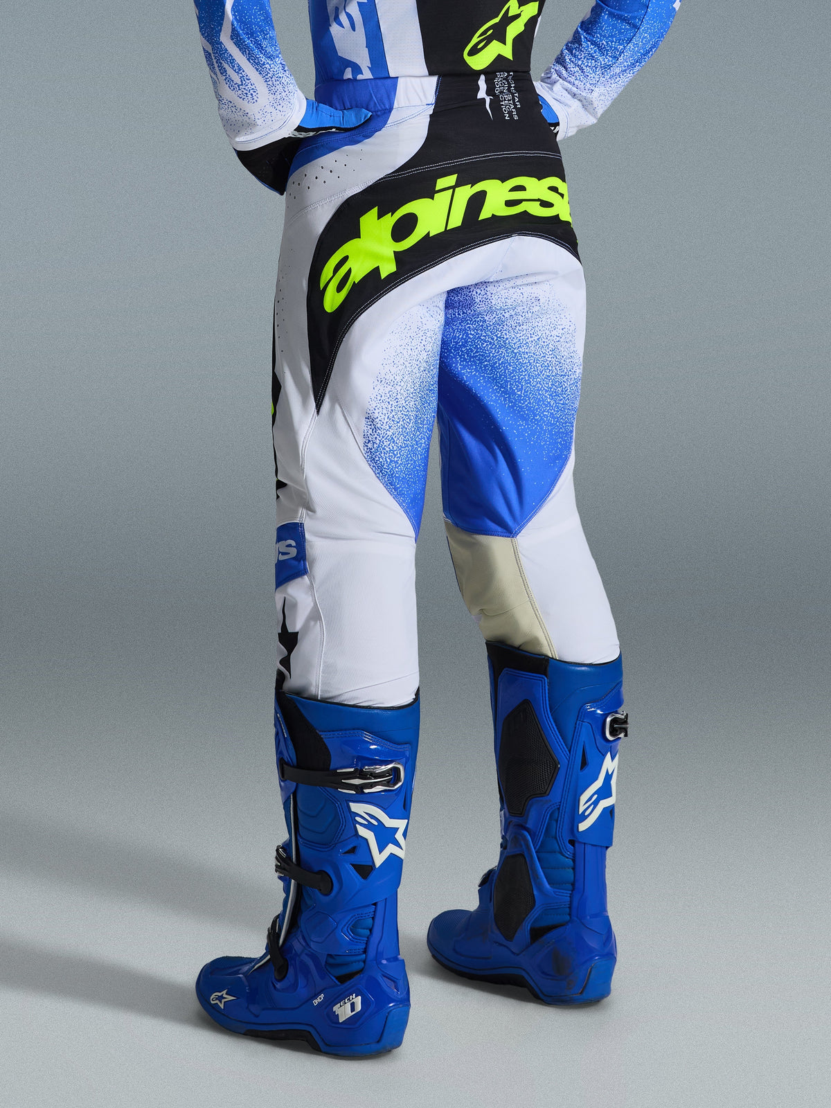 Alpinestars 2026 Techstar Knif Pants, Motocross Pants, Ucla Blue Black and Yellow Fluo, rear view showing a bold neon yellow Alpinestars logo across the back, white chassis with blue gradient graphics, worn with high-performance bright blue motocross boots.