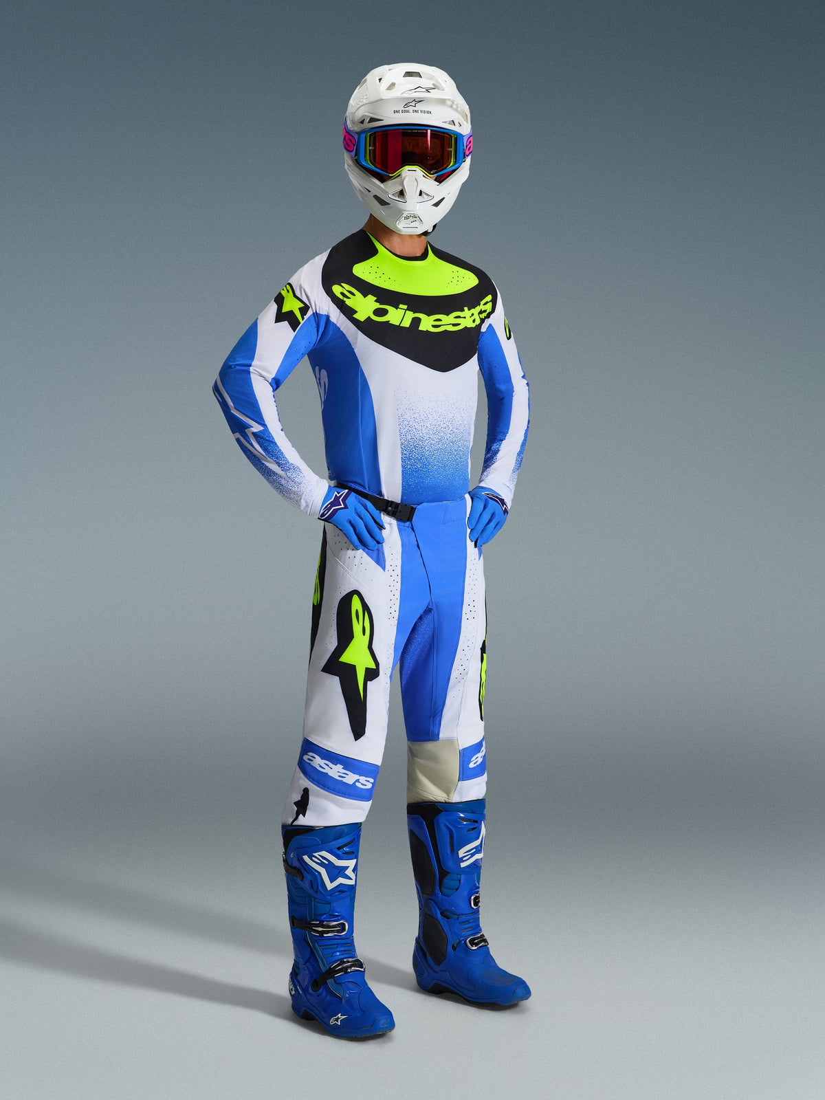 Motocross rider wearing Alpinestars 2026 Techstar Knif Pants in Ucla Blue, Black, and Yellow Fluo, full racing gear set with matching jersey featuring bold Alpinestars branding, blue boots, white helmet with goggles, and blue gloves, athletic stance for off-road performance
