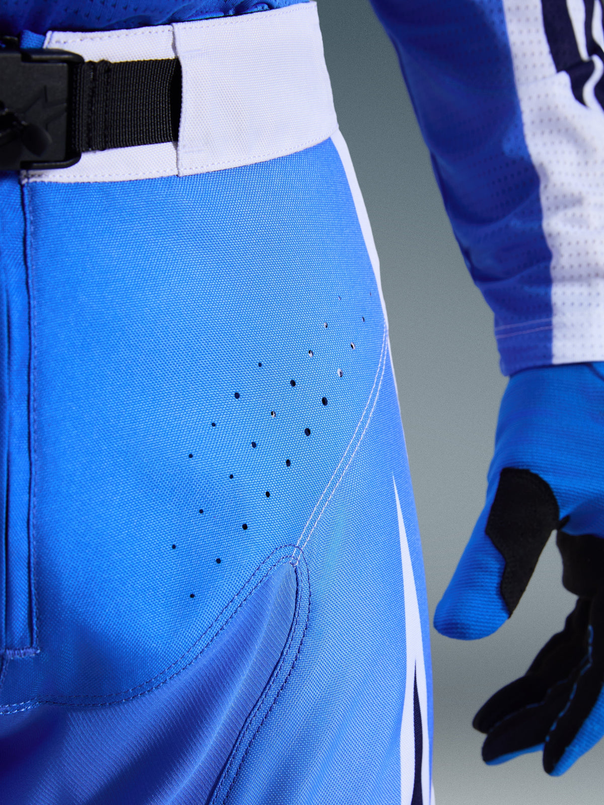 Alpinestars 2026 Techstar Knif Pants, Ucla Blue and White, close-up of hip area showing laser-cut perforations for ventilation, SX2 magnetic buckle waist closure, and matching motocross gloves