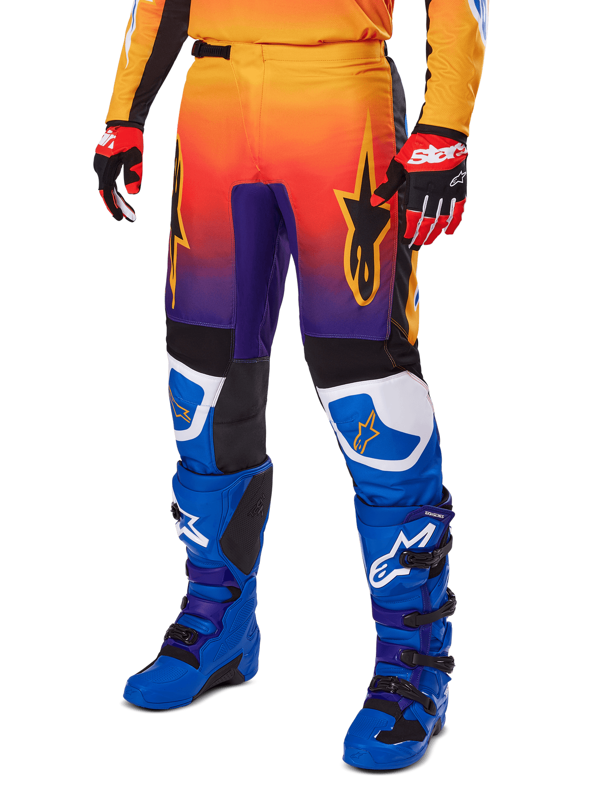 Alpinestars 2025 Fluid Wurx Pants, spodnie motocrossowe, wielokolorowy gradient pomarańczowo-czerwony i fioletowy z czarnymi i niebieskimi panelami, noszone z niebieskimi butami i czerwonymi rękawicami, grafiki z logo gwiazdy i białe akcenty na kolanach, wytrzymała odzież wyczynowa do wyścigów terenowych