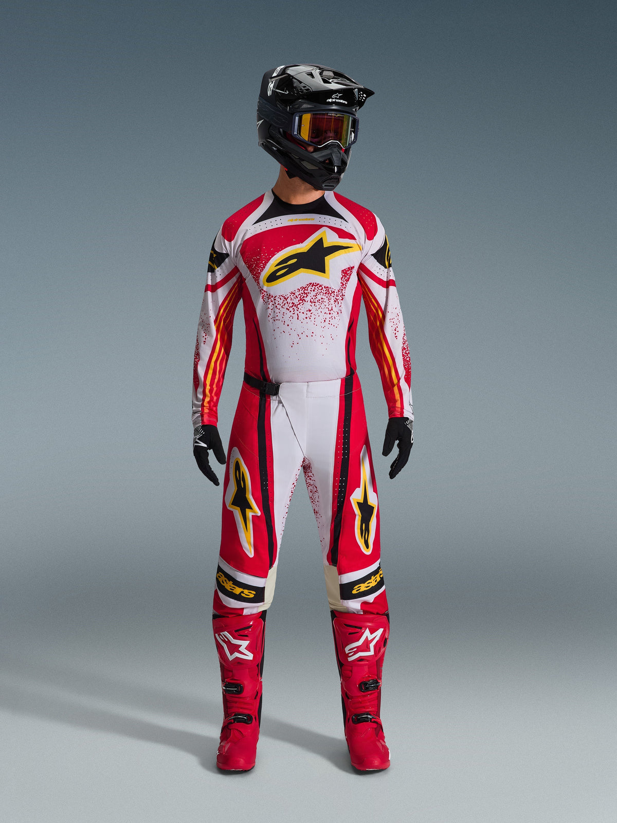 Koszulka Alpinestars Techstar Nomur 2026, czerwono-biała z czarnymi akcentami i żółtym logo, noszona przez zawodnika motocrossowego z dopasowanymi spodniami, czerwonymi butami i czarnym kaskiem, profesjonalna odzież do wyścigów terenowych