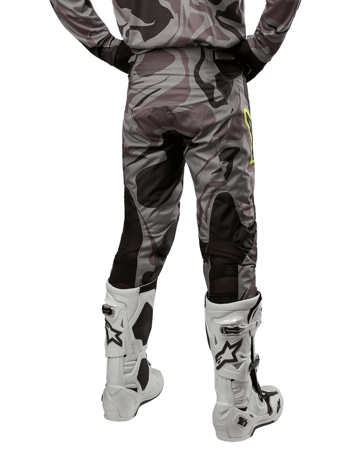 Alpinestars 2024 Racer Tactical Pants, spodnie motocrossowe, kolor Cast Gray Camo Magnet, widok z tyłu ukazujący wzór kamuflażu i czarne, oddychające strefy elastyczne, noszone z biało-czarnymi butami motocrossowymi, zaprojektowane do wyścigów terenowych.