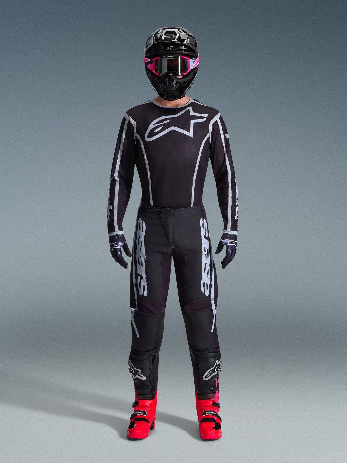 Zestaw Alpinestars 2026 Fluid Apex, strój motocrossowy, czarny z szarymi akcentami, koszulka z dużym białym logo Astars, pasujące spodnie z wyraźnym brandingiem, czarny kask z różowymi goglami, jaskrawoczerwone buty, kompletny zestaw do wyścigów off-road