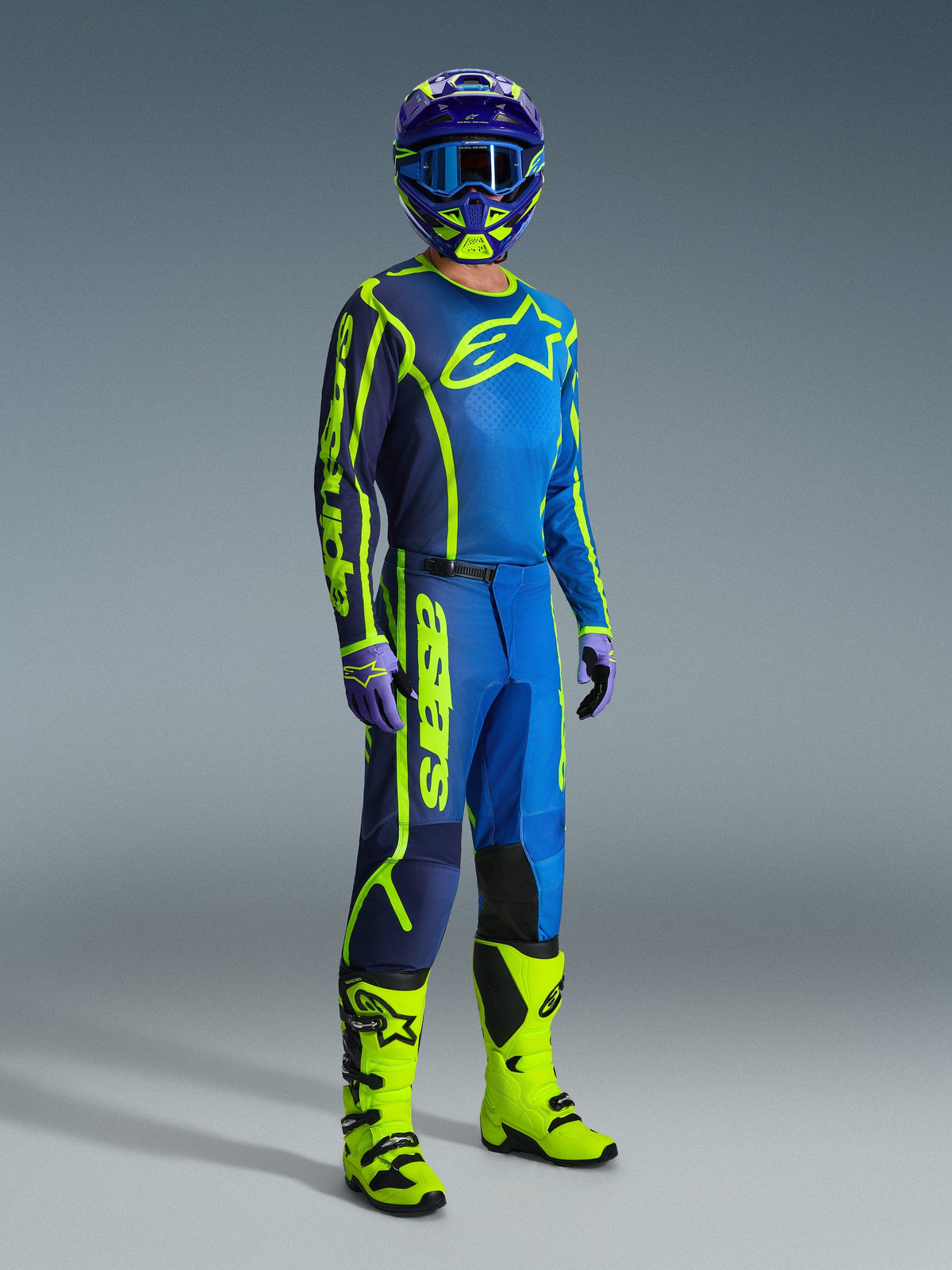 Motocross rider wearing Alpinestars 2026 Fluid Apex Pants in Blue and Yellow Fluo, coordinated with a matching jersey, blue and yellow helmet, and vibrant yellow boots, professional off-road gear set for motocross.