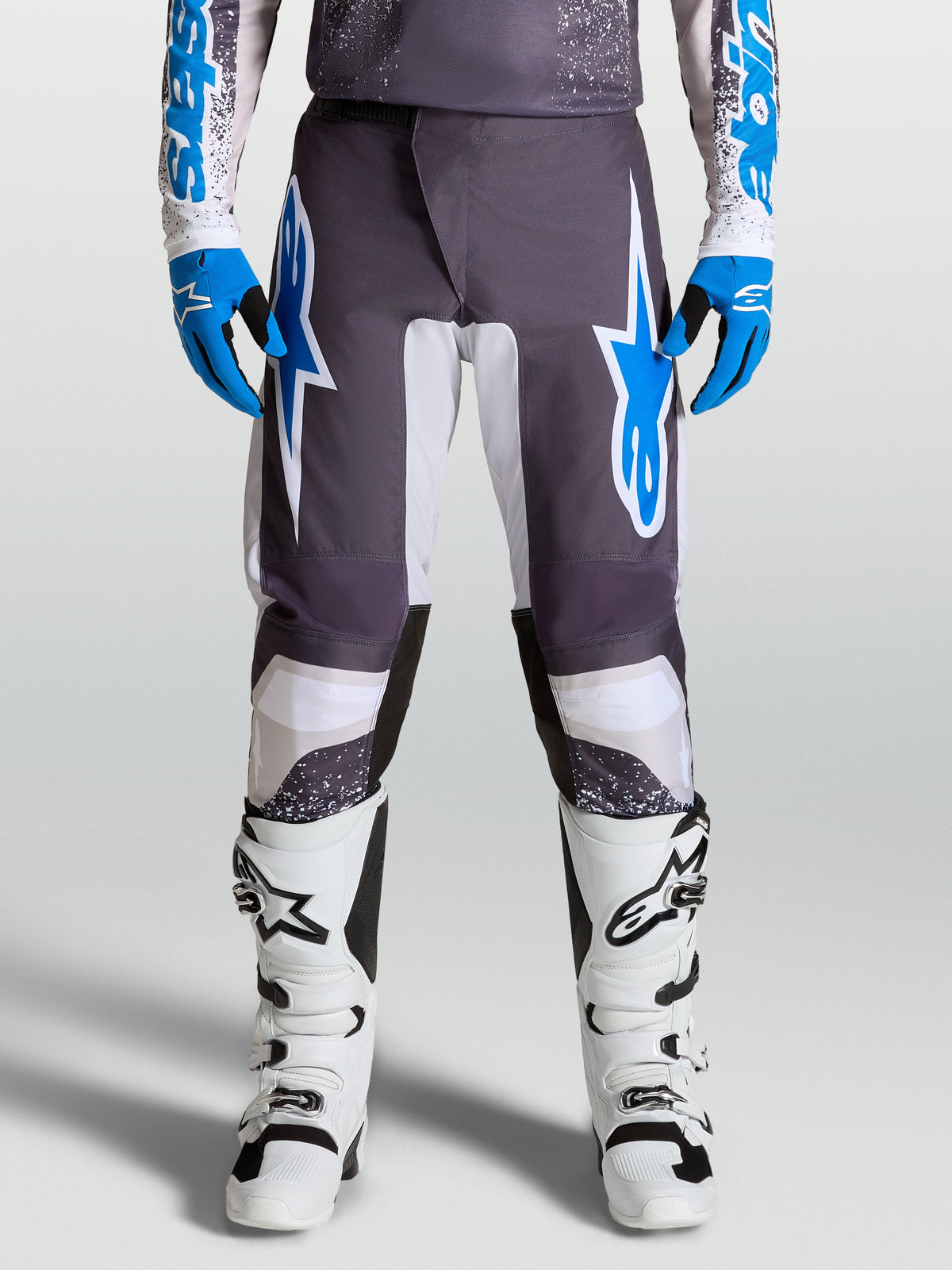 Spodnie Alpinestars Fluid Drag, motocrossowe, szare i niebieskie, profilowane nogawki i wzmocnienia z polytkaniny, na modelu.