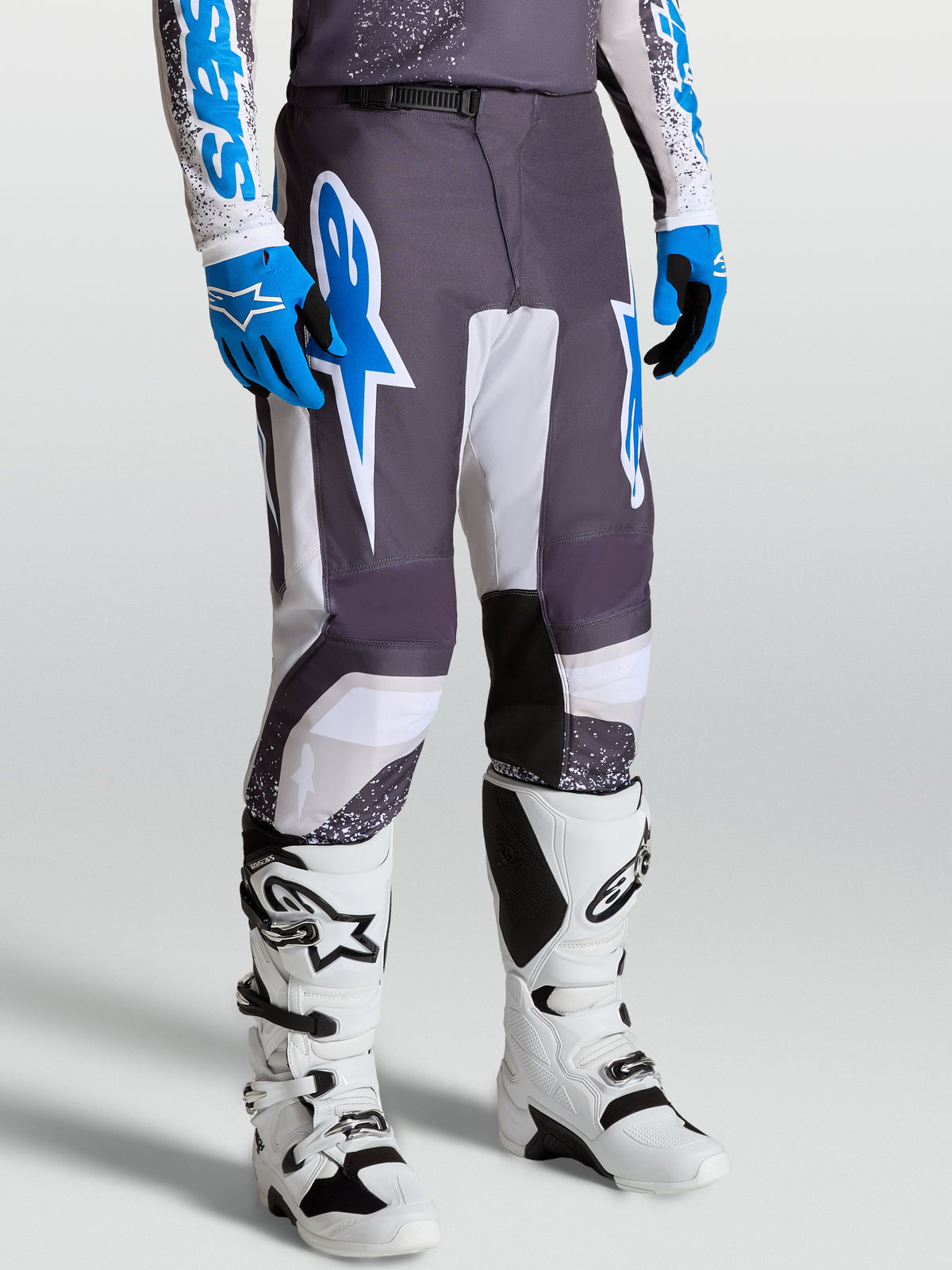 Alpinestars Spodnie Fluid Drag, męskie spodnie motocrossowe wyścigowe, szare, białe i niebieskie, ergonomiczny sportowy krój, widok na modela w butach.