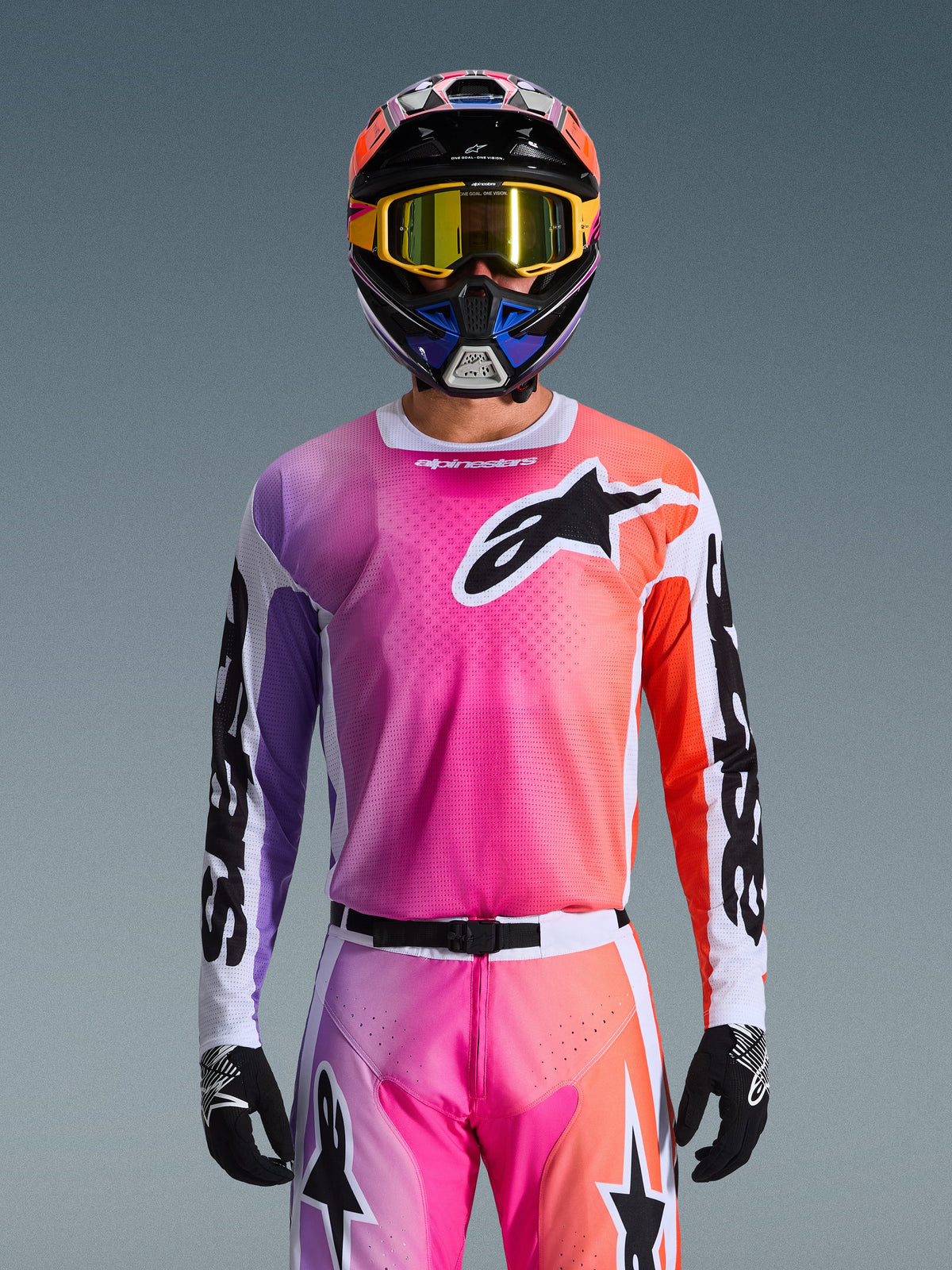 Alpinestars 2026 Racer Air Portl Jersey, koszulka motocrossowa, jaskrawy gradient w kolorach różowym, fioletowym i pomarańczowym, noszona z pasującym kaskiem i goglami, z dużym czarnym logo z gwiazdą na klatce piersiowej, oddychająca konstrukcja z siatki, odzież wyczynowa do jazdy off-road