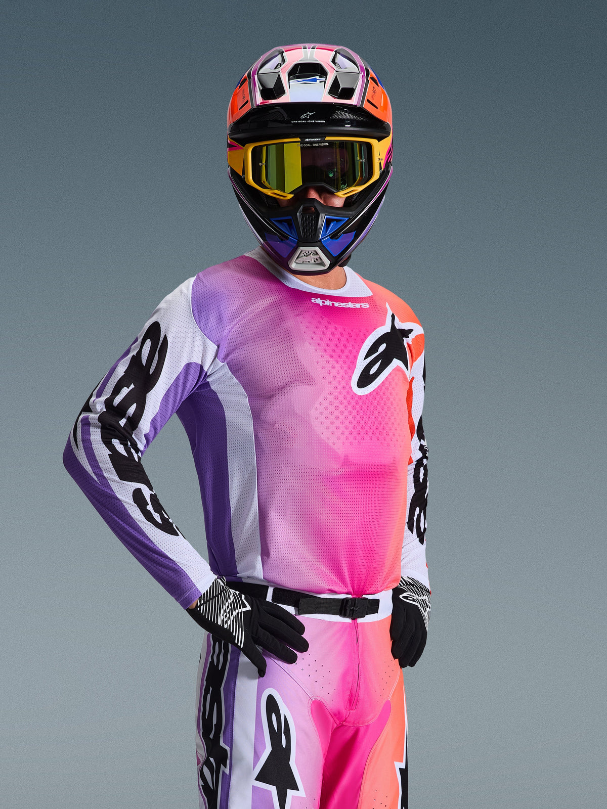 Zawodnik motocrossowy w koszulce Alpinestars 2026 Racer Air Portl, różowo-fioletowo-pomarańczowy gradient z białymi akcentami, pasujący kolorowy kask i żółte gogle, czarne rękawice, profesjonalny sprzęt do wyścigów off-road