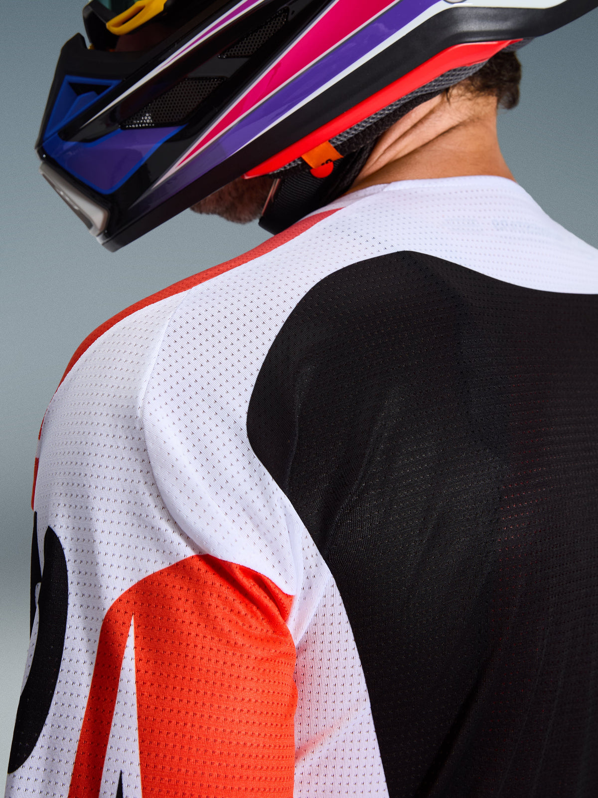 Alpinestars 2026 Racer Air Portl Jersey, koszulka motocrossowa, wielokolorowa z białymi, czarnymi i czerwonymi panelami, zbliżenie na perforowaną konstrukcję z siatki na ramieniu i plecach zapewniającą wentylację, noszona z kolorowym kaskiem motocrossowym