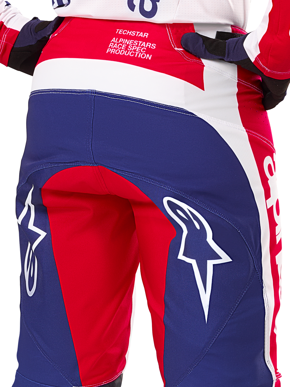 Spodnie Alpinestars Limited Edition Techstar Fortitude, spodnie motocrossowe, czerwone, białe i niebieskie, widok z tyłu z dużymi białymi logo gwiazdy na siedzisku oraz brandingiem Techstar Race Spec, wytrzymałe tekstylia techniczne do wyścigów off-road