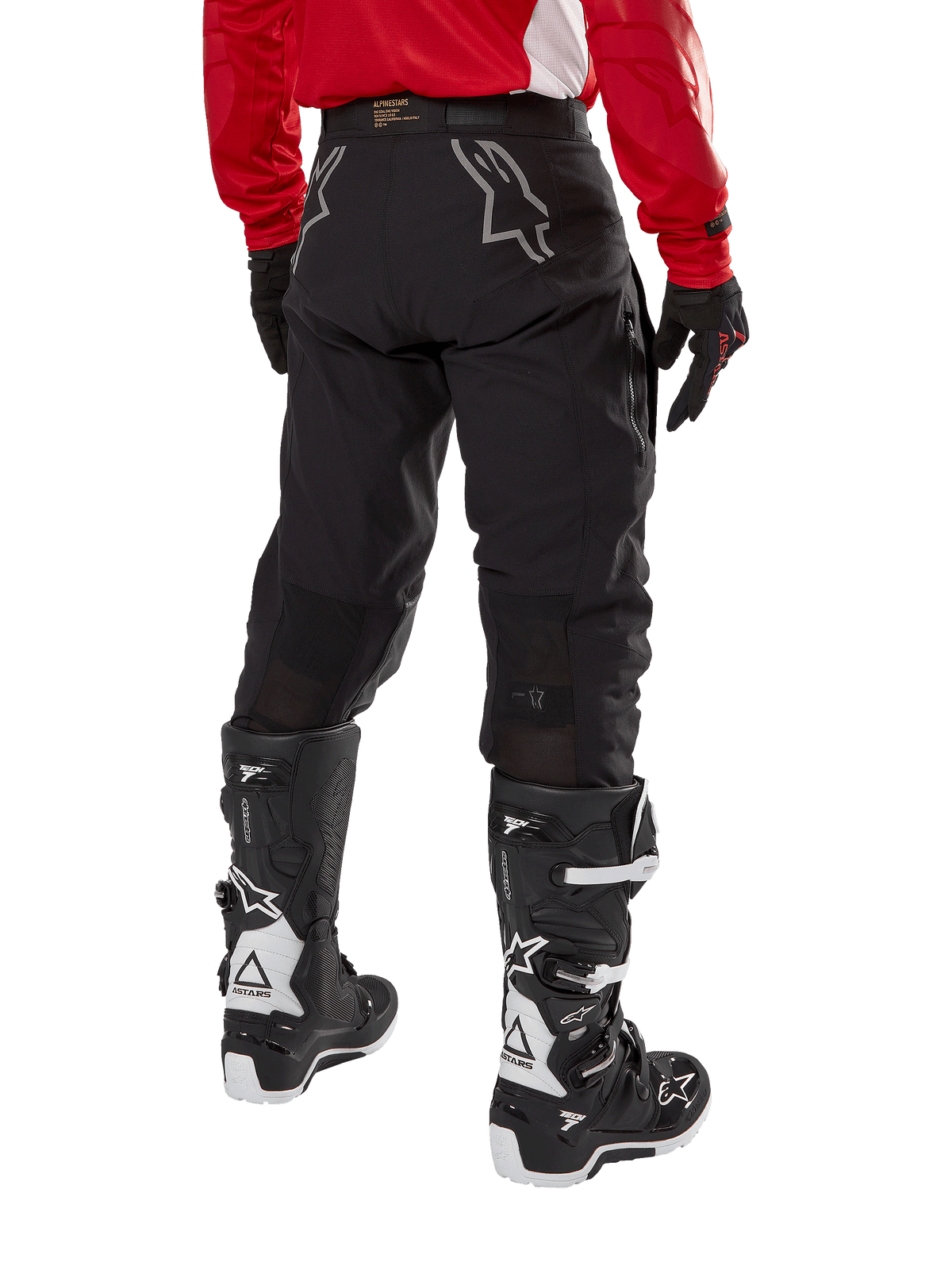 Alpinestars Techdura Pants, spodnie enduro off-road, czarne, widok z tyłu pokazujący szare logo gwiazdy na siedzeniu, noszone z czerwoną koszulką z długim rękawem i czarno-białymi butami Tech 7, wytrzymała konstrukcja tekstylna do jazdy typu adventure