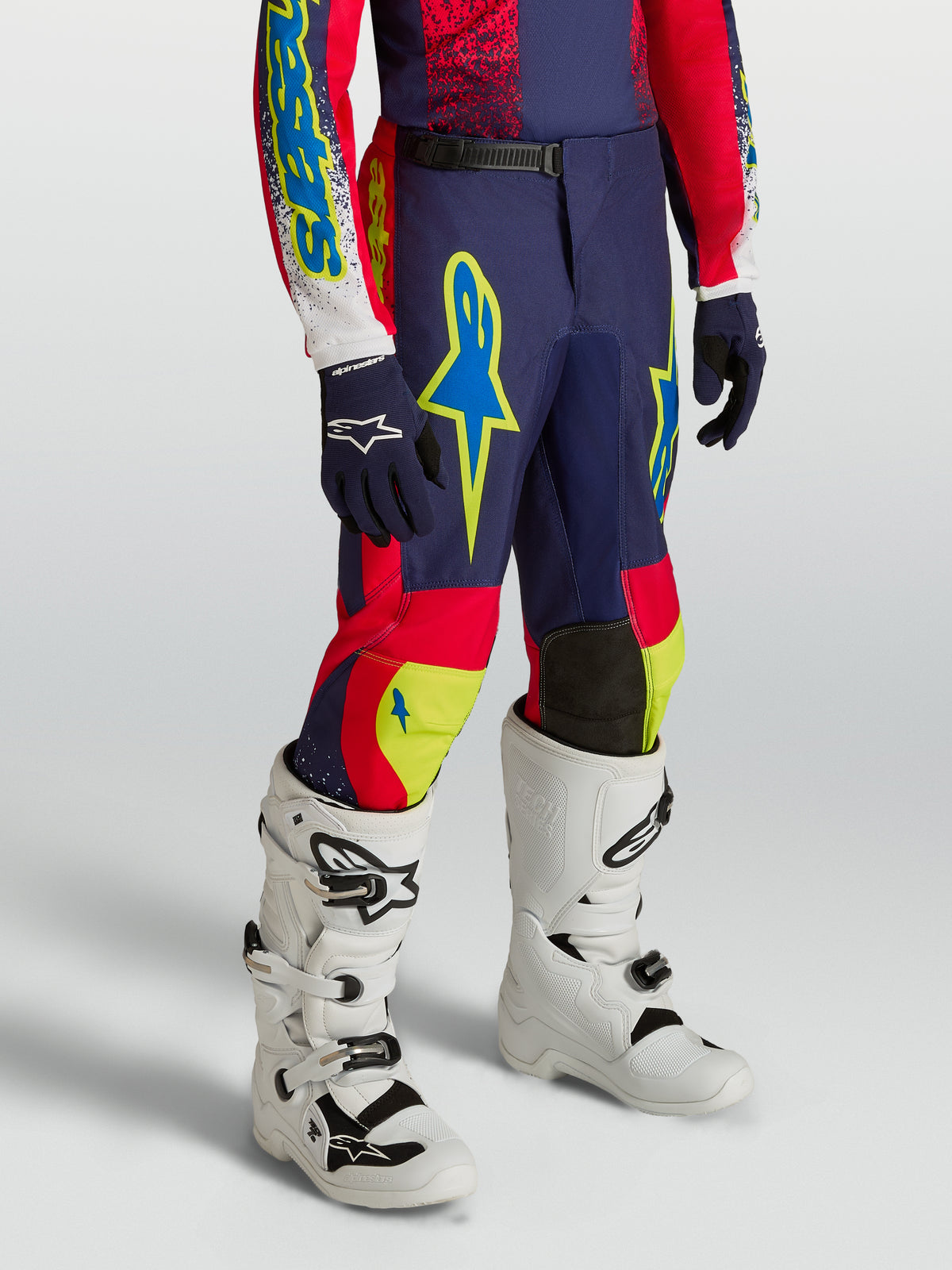Alpinestars Fluid Drag, młodzieżowe spodnie motocrossowe, granatowo-czerwone z neonowymi detalami i białymi butami.