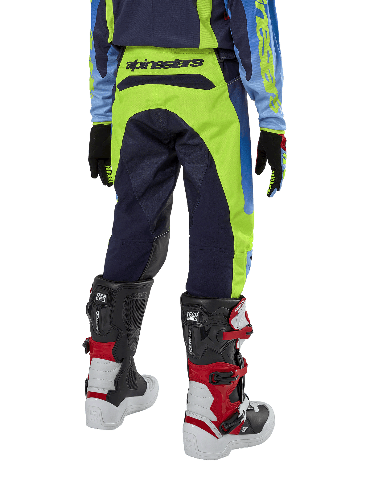 Alpinestars Youth 2024 Racer Hoen Pants, spodnie motocrossowe, żółte fluo i granatowe, widok z tyłu prezentujący wyraźne logo Alpinestars na pasie, noszone z czarno-czerwonymi butami Tech Series i pasującą koszulką, wytrzymały sportowy krój do jazdy terenowej dla młodzieży