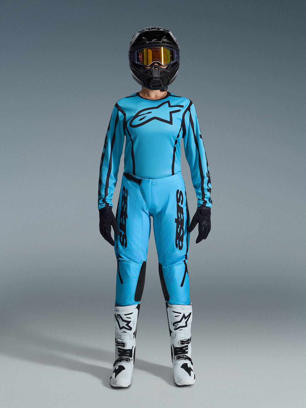 Zestaw Alpinestars 2026 Stella Fluid Apex, damska koszulka i spodnie motocrossowe, niebieski i czarny, z dużym logo gwiazdy na klatce piersiowej, noszony z czarnym kaskiem, przyciemnianymi goglami i białymi butami z czarnymi akcentami, kompletny strój wyścigowy off-road