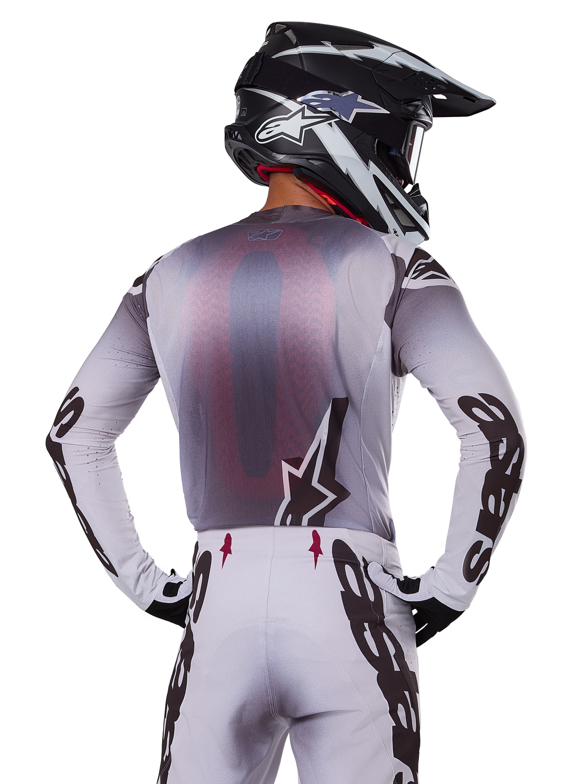 Alpinestars 2025 Supertech Maker Gear Set, motocross rider shown from the back, white and gray jersey with large black branding on sleeves and star logo, matching white pants with black graphics, black and white helmet, professional off-road racing outfit