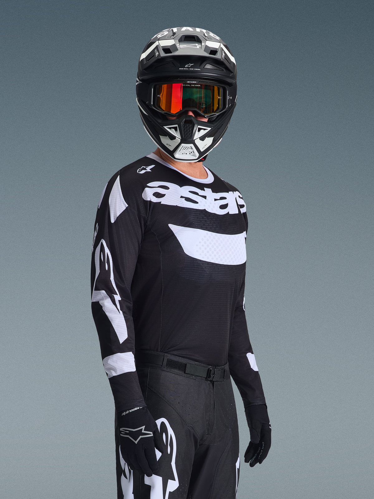 Motocyklista motocrossowy w koszulce 2026 Racer Air Riway, czarno-biała koszulka z logo „astars”, dopasowany czarno-biały kask z pomarańczowymi lustrzanymi goglami, czarne spodnie i rękawice motocrossowe, skoordynowany strój do wyścigów off-road