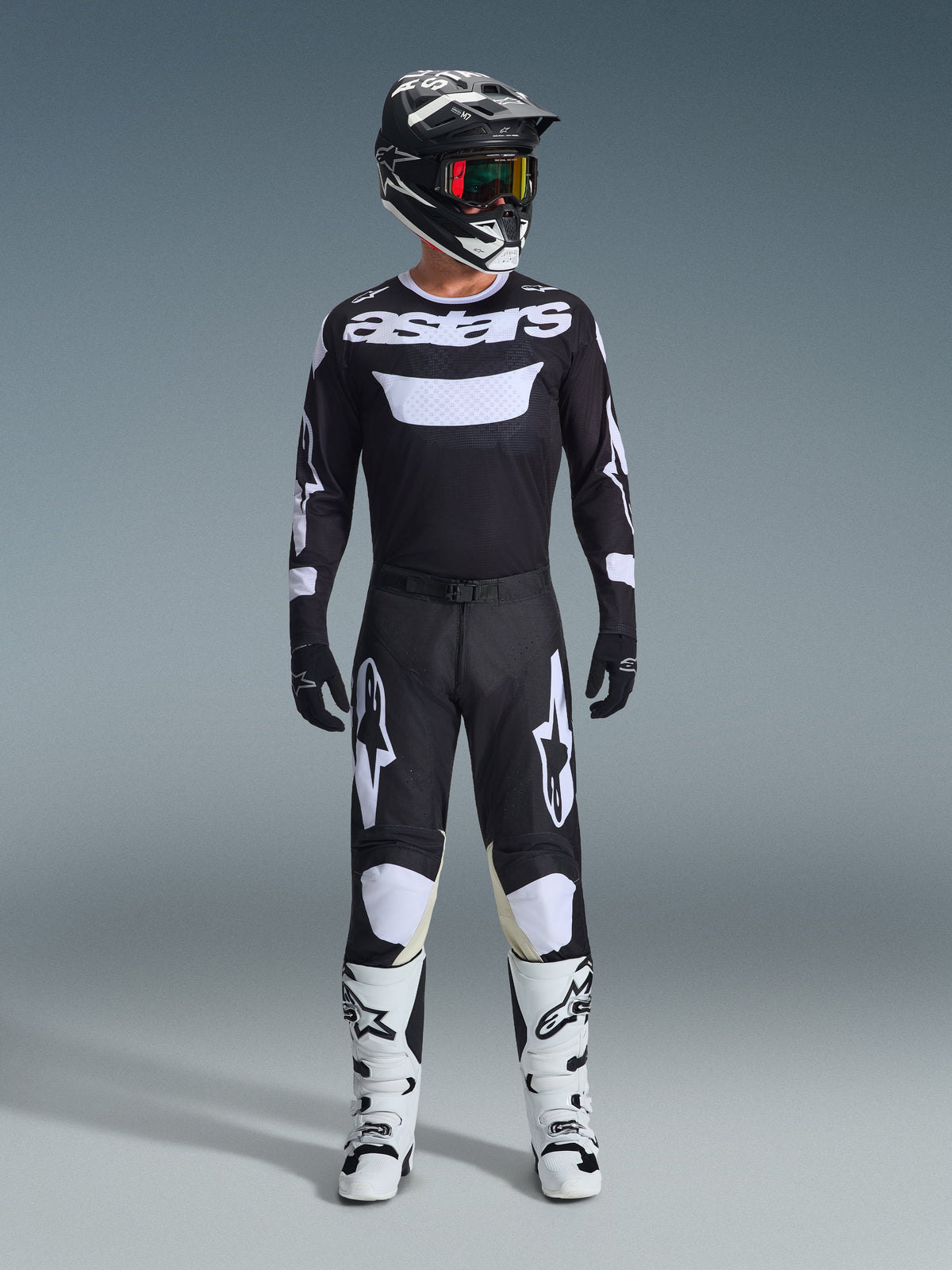 Zawodnik motocrossowy w pełnym stroju wyścigowym, koszulka Alpinestars 2026 Racer Air Riway w kolorze czarno-białym z brandingiem 'astars' na klatce piersiowej, pasujące czarne spodnie z białymi akcentami, białe buty motocrossowe oraz czarno-biały kask z goglami, profesjonalny zestaw do jazdy off-road