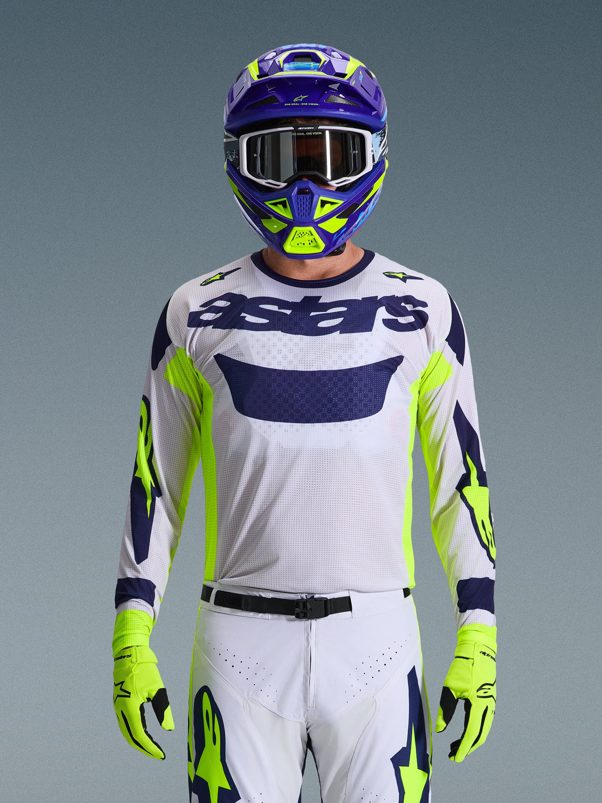 Alpinestars 2026 Racer Air Riway Jersey, jasnoszara koszulka motocrossowa z ciemnoniebieskim logo astars, neonowożółte i niebieskie akcenty na rękawach, noszona przez motocyklistę z dopasowanym fioletowym i neonowożółtym kaskiem oraz rękawicami, techniczna tkanina siatkowa do wyścigów off-road