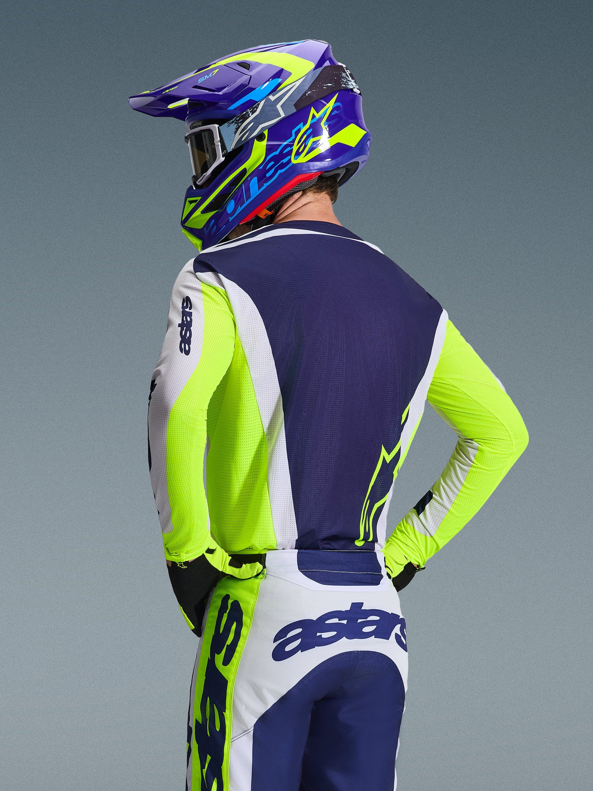 Alpinestars 2026 Racer Air Riway Jersey, koszulka motocrossowa, jasnoszara, neonowo-żółta i niebieska, widok z tyłu na motocyklistę w pasujących spodniach i kasku, sportowy krój wyścigowy z oddychającymi panelami z siatki do jazdy off-road