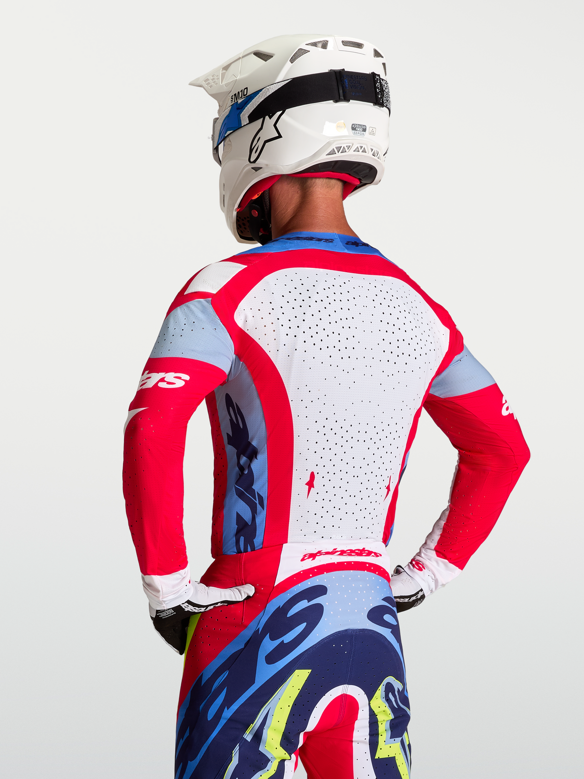 Alpinestars Koszulka Supertech Dyna, męska koszulka motocrossowa, czerwona i biała, oddychający perforowany panel siatkowy na plecach, widok z tyłu na zawodnika w kasku.