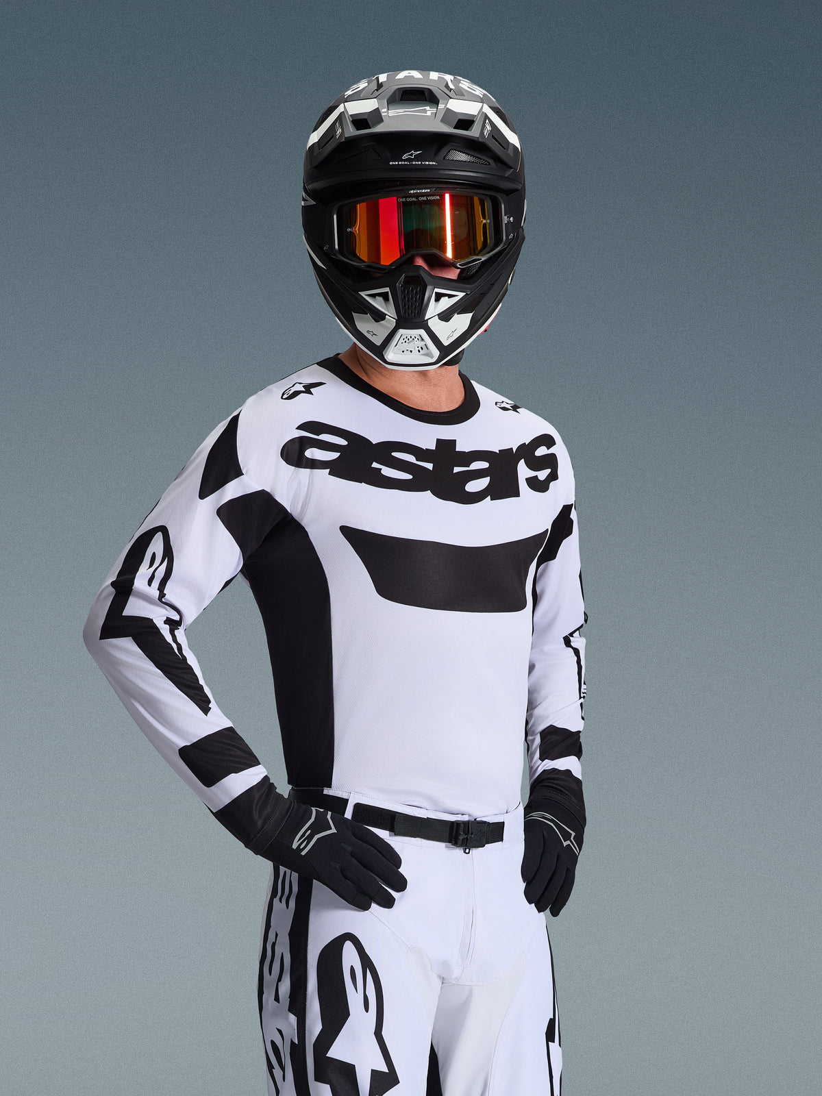 Koszulka Alpinestars Racer Riway 2026, koszulka motocrossowa, biało-czarna, z wyraźnym logo „astars” na piersi, zestawiona z pasującymi białymi spodniami i czarnymi rękawicami, czarno-biały kask z czerwonymi lustrzanymi goglami, profesjonalna odzież wyścigowa off-road