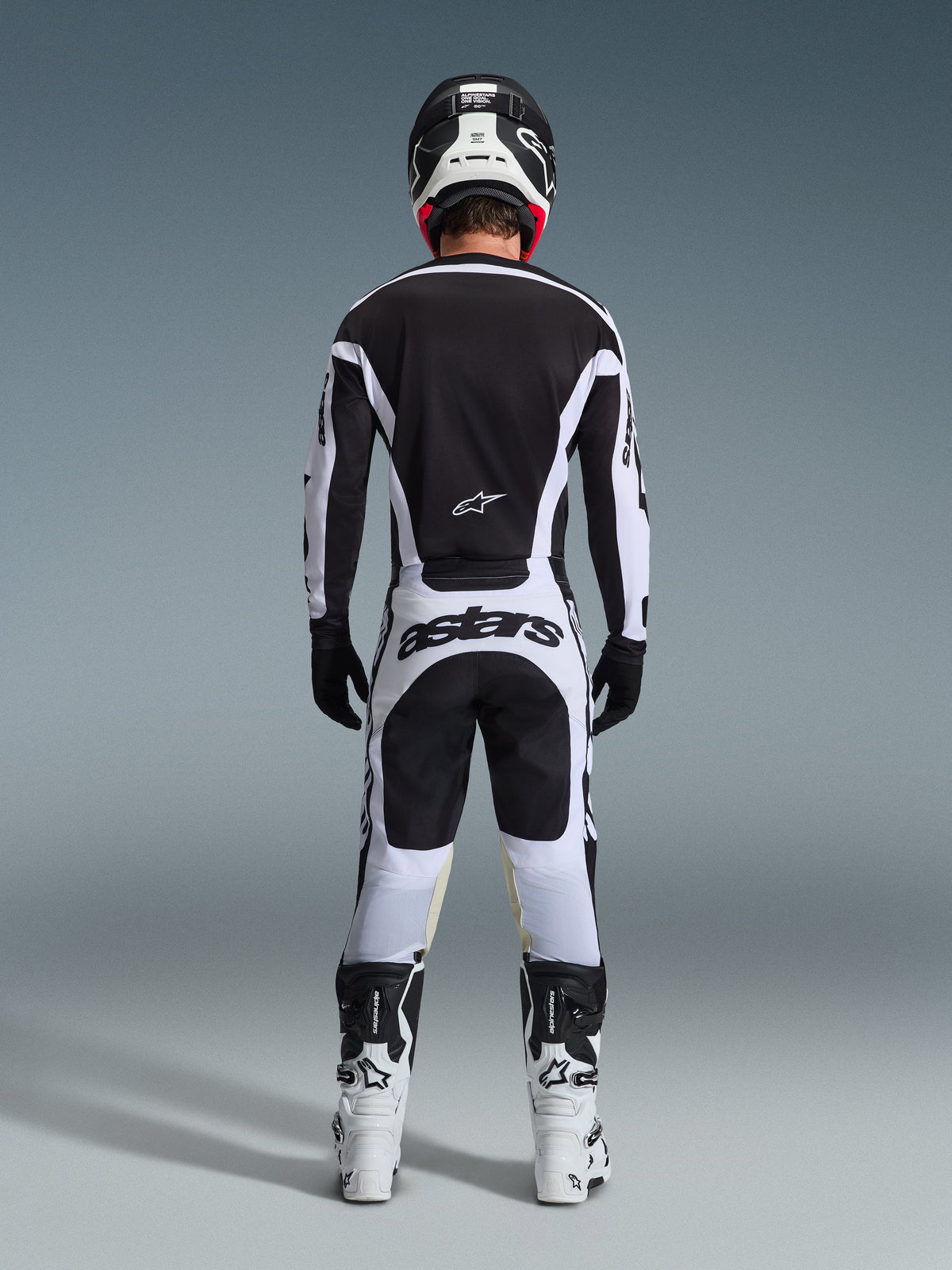Motocyklista motocrossowy widoczny od tyłu w pełnym stroju wyścigowym, koszulka 2026 Racer Riway w kolorze biało-czarnym, pasujące spodnie z logo „astars” na siedzeniu, czarny kask z białymi detalami, czarne rękawice i biało-czarne buty, profesjonalny zestaw off-road