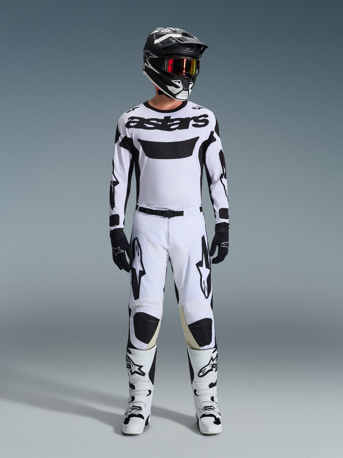 Koszulka Alpinestars 2026 Racer Riway, koszulka motocrossowa, biało-czarna, noszona jako kompletny zestaw wyścigowy z pasującymi spodniami, czarnym kaskiem z czerwonymi goglami, czarnymi rękawicami i białymi butami, z wyrazistym czarnym brandingiem „astars” i logo gwiazdy.