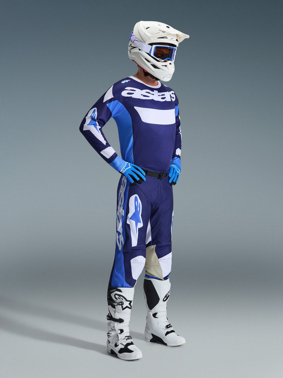 Koszulka Alpinestars 2026 Racer Riway w kolorze Ucla Blue i białym, noszona przez zawodnika motocrossowego wraz z dopasowanymi spodniami, białym kaskiem, niebieskimi rękawicami i białymi butami, z wyraźnym brandingiem 'astars' na klatce piersiowej, kompletny strój wyścigowy off-road