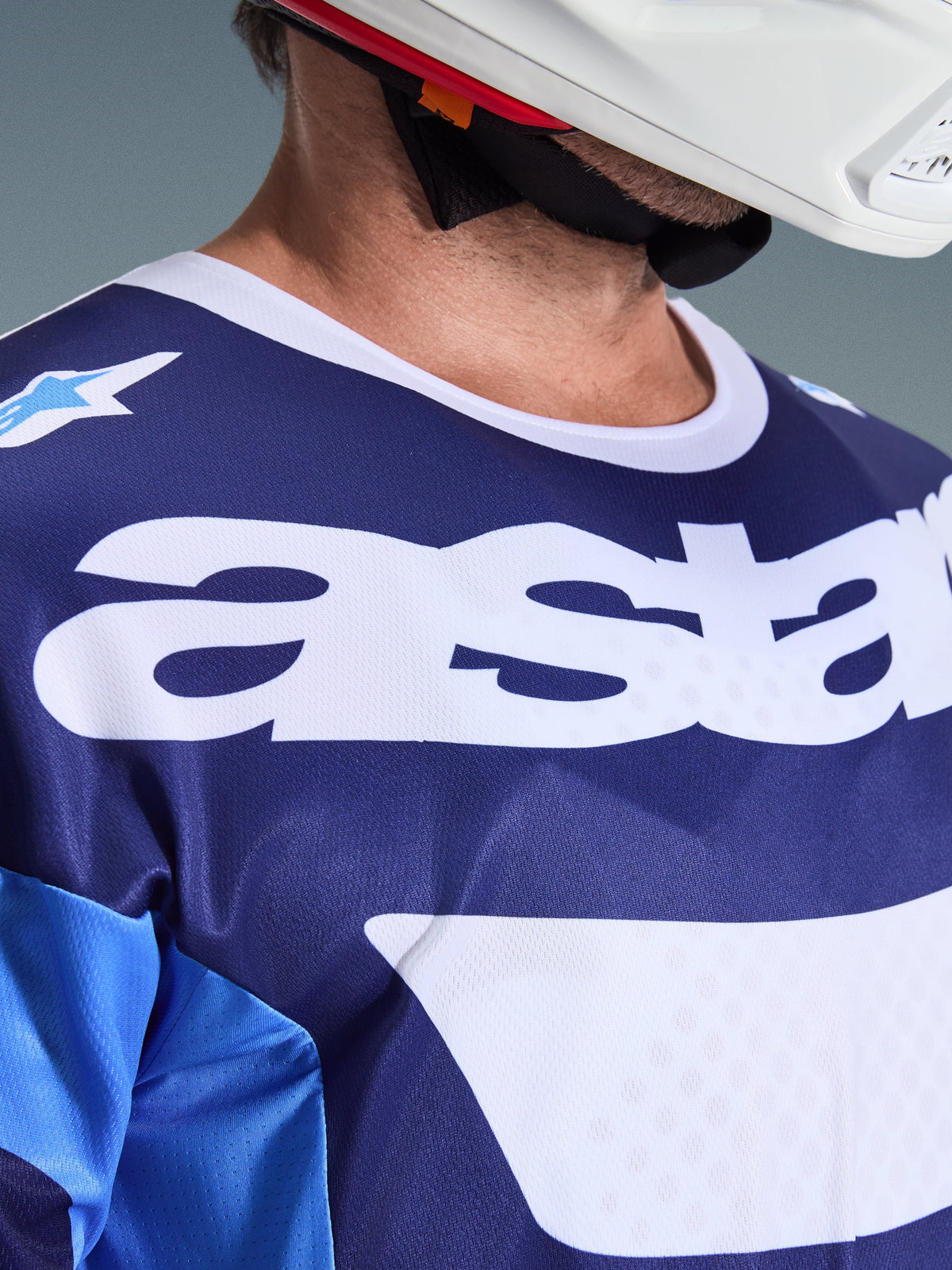 Alpinestars 2026 Racer Riway Jersey, Motocross Jersey, Ucla Blue and White, close-up view of chest featuring large white 'astars' branding, white collar, and moisture-wicking mesh texture, worn with a white helmet