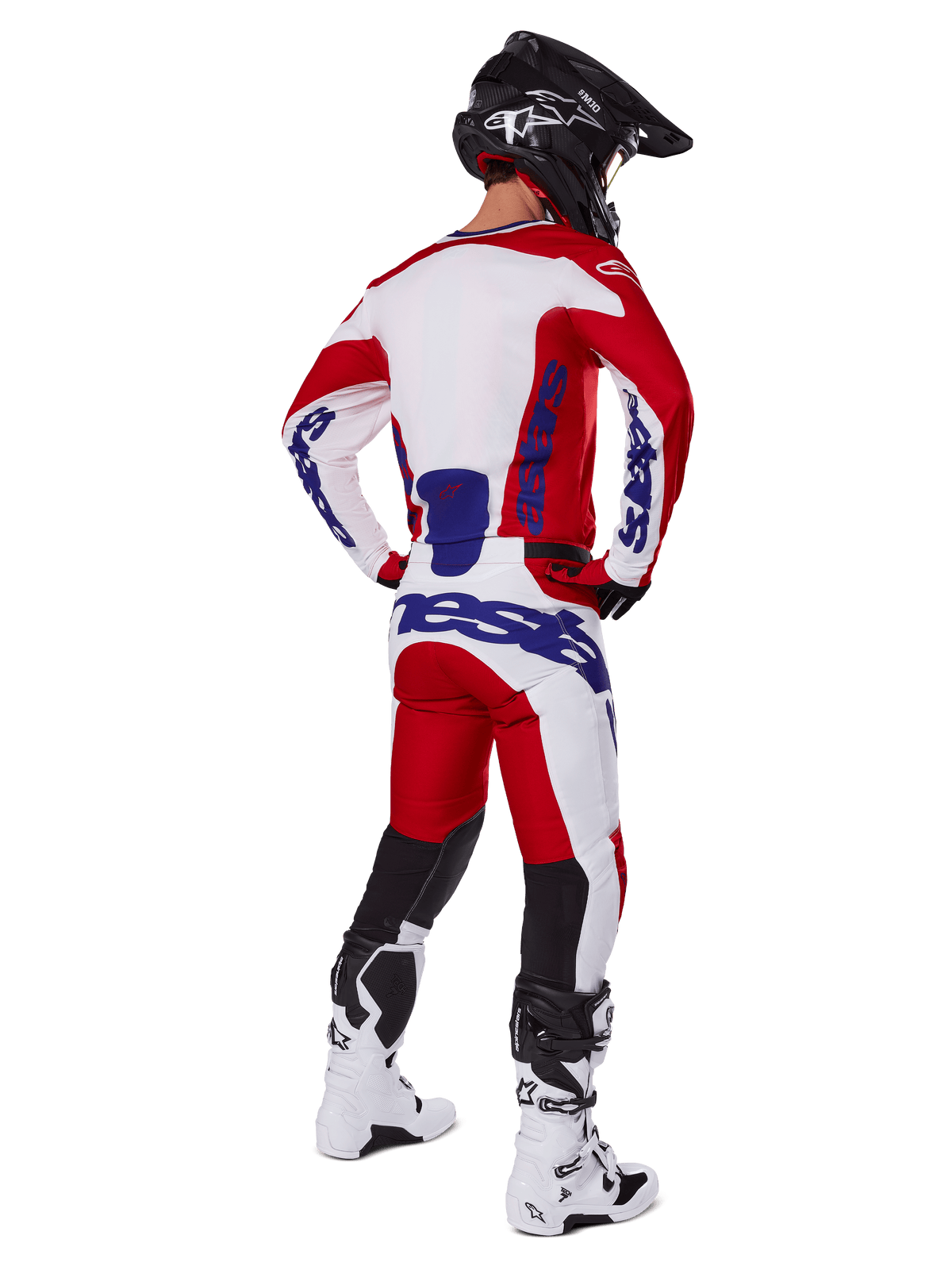 Motocyklista motocrossowy widoczny od tyłu, ubrany w koszulkę i spodnie Alpinestars 2025 Racer Veil w kolorze czerwonym i białym, niebieski branding, czarny kask i białe buty, kompletny zestaw odzieży do wyścigów terenowych