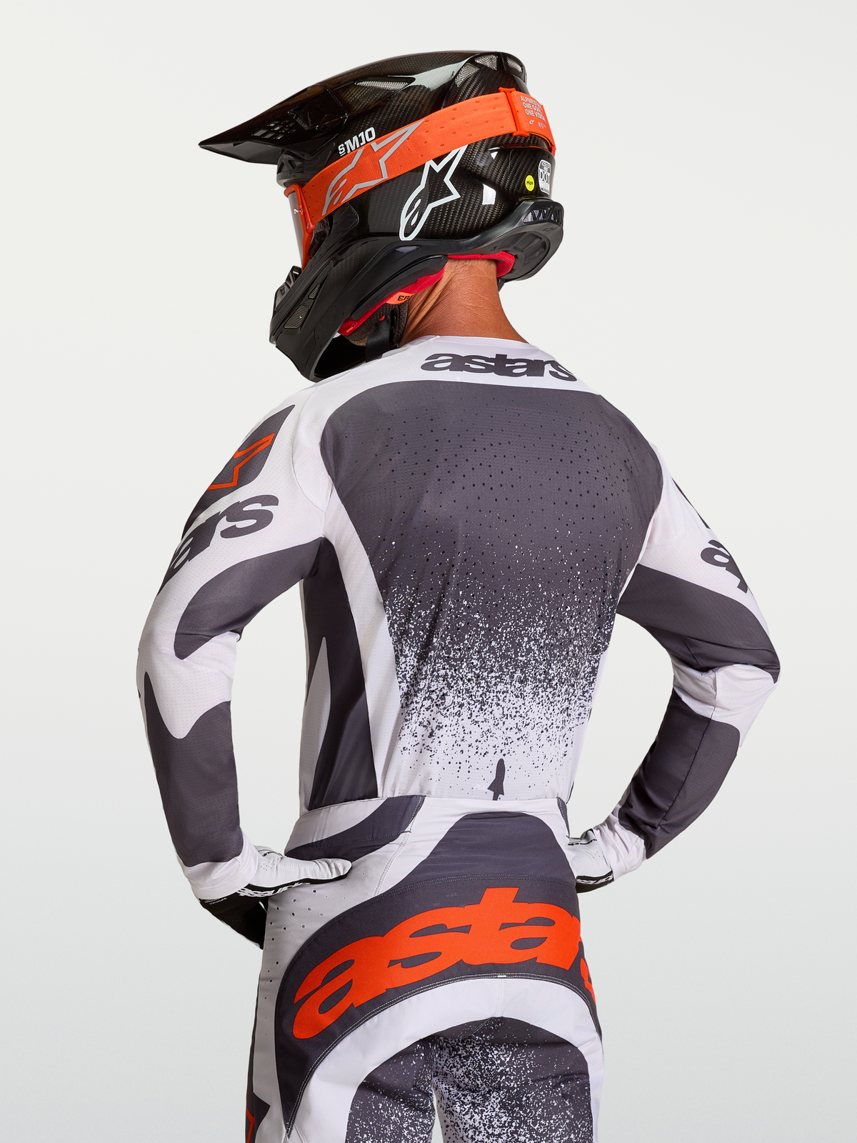 Koszulka motocrossowa Alpinestars Techstar Swan, męska, szaro-biała z czerwonymi detalami, widok z tyłu na motocykliście, sportowy krój wyścigowy z laserowymi perforacjami i logo astars na plecach.