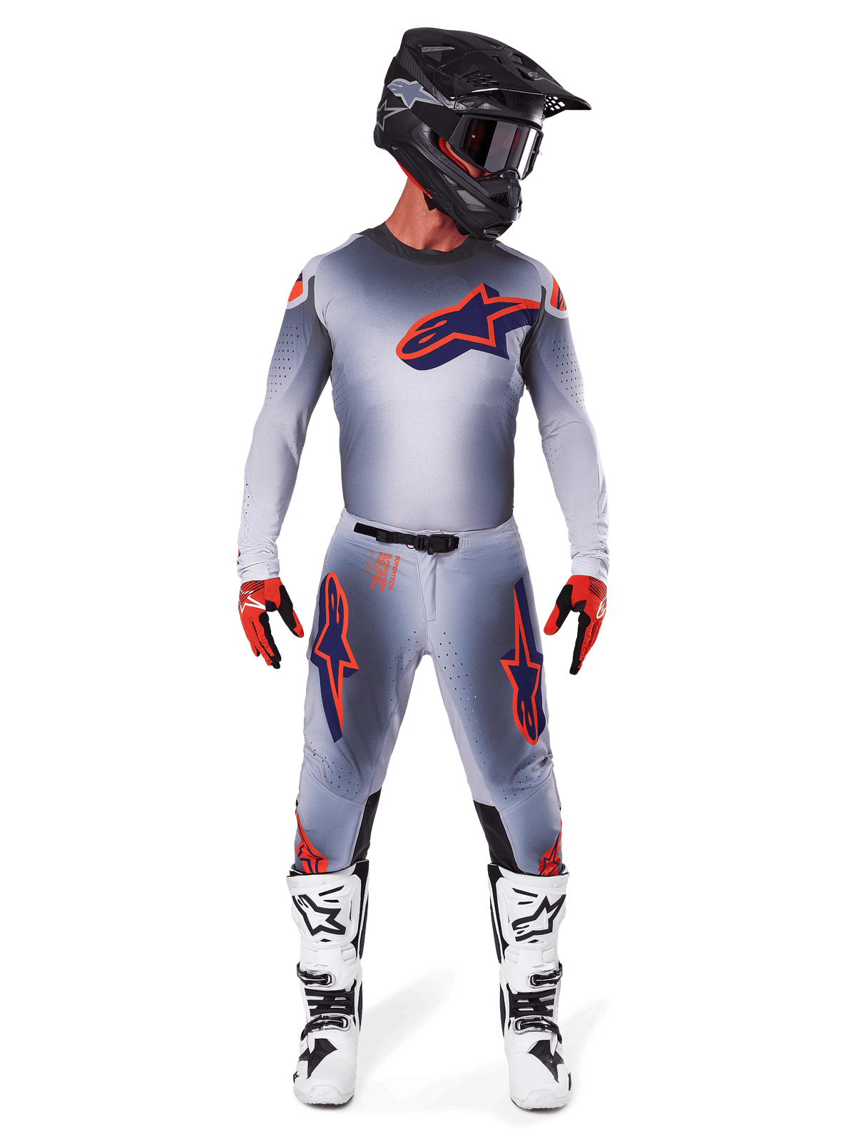 Zawodnik motocrossowy w koszulce Alpinestars 2025 Supertech Lipan w kolorze Gray Orange Fluo, szary gradient i pomarańczowe logo, w zestawie z dopasowanymi spodniami motocrossowymi, czarnym kaskiem, białymi butami i pomarańczowymi rękawicami, profesjonalny zestaw wyścigowy.