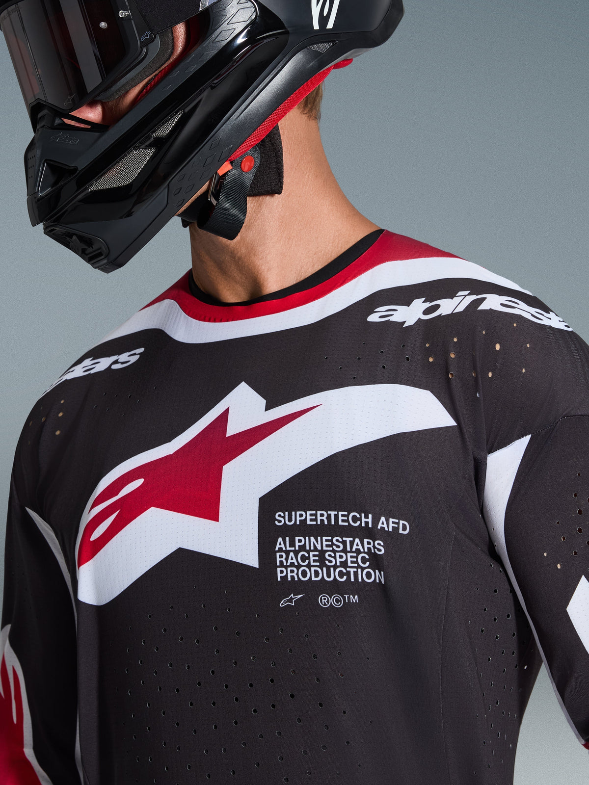 Alpinestars 2026 Supertech AFD Vista Jersey, Black Red and White, close-up of chest showing Alpinestars star logo and 'Supertech AFD' text, featuring laser-cut ventilation holes and mesh construction, worn with black motocross helmet.