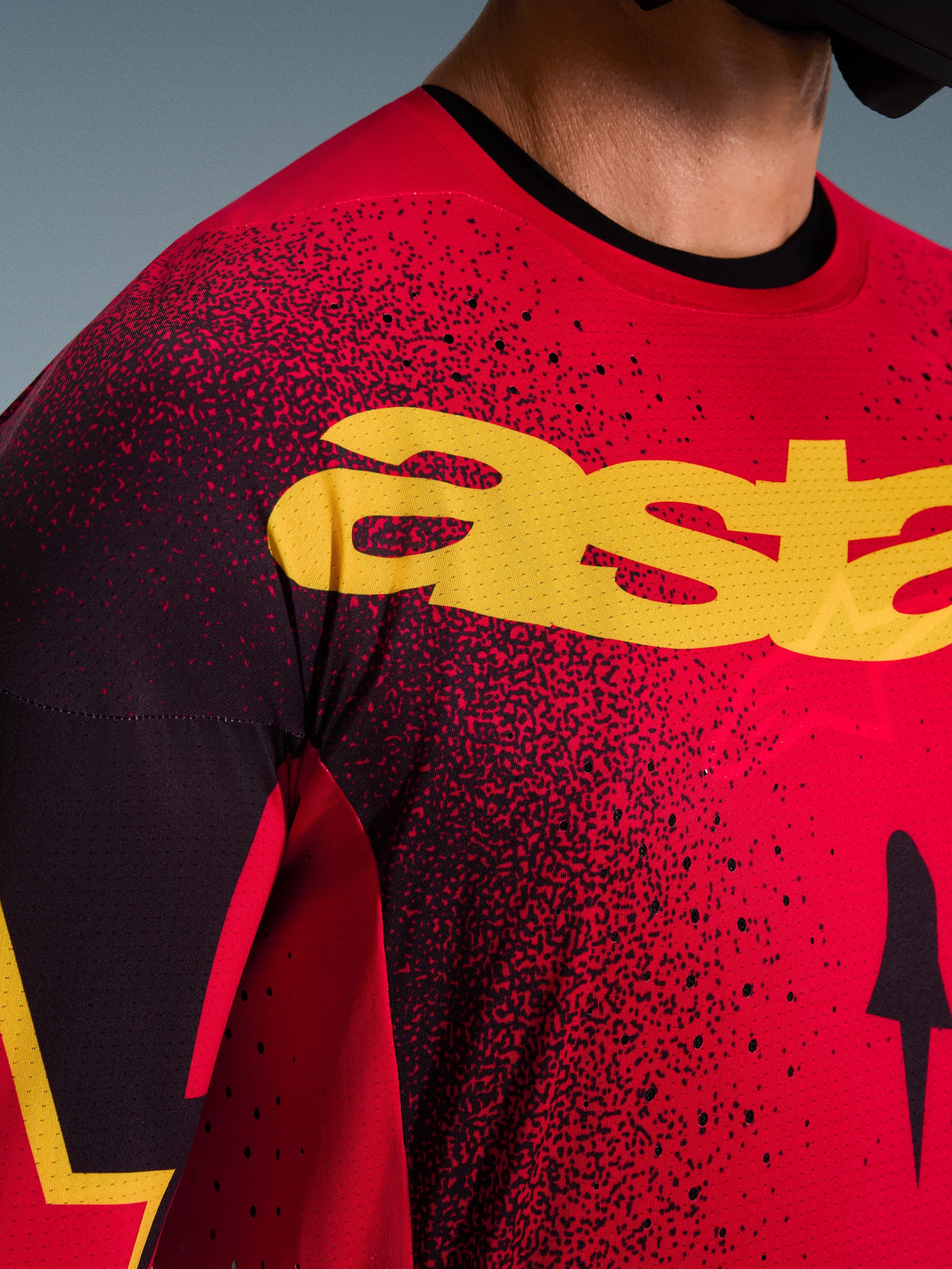 Alpinestars Supertech Scenz Jersey 2026, koszulka motocrossowa, czerwona, czarna i żółta, zbliżenie na klatkę piersiową z żółtym brandingiem, czarnym nakrapianym wzorem i laserowo wycinanymi perforacjami zapewniającymi wentylację